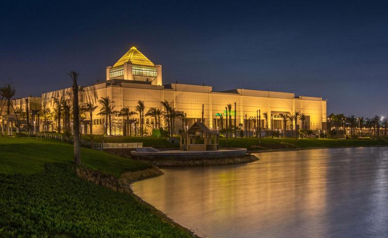 NMEC building illuminated at night with golden pyramid roof reflecting on a calm lake