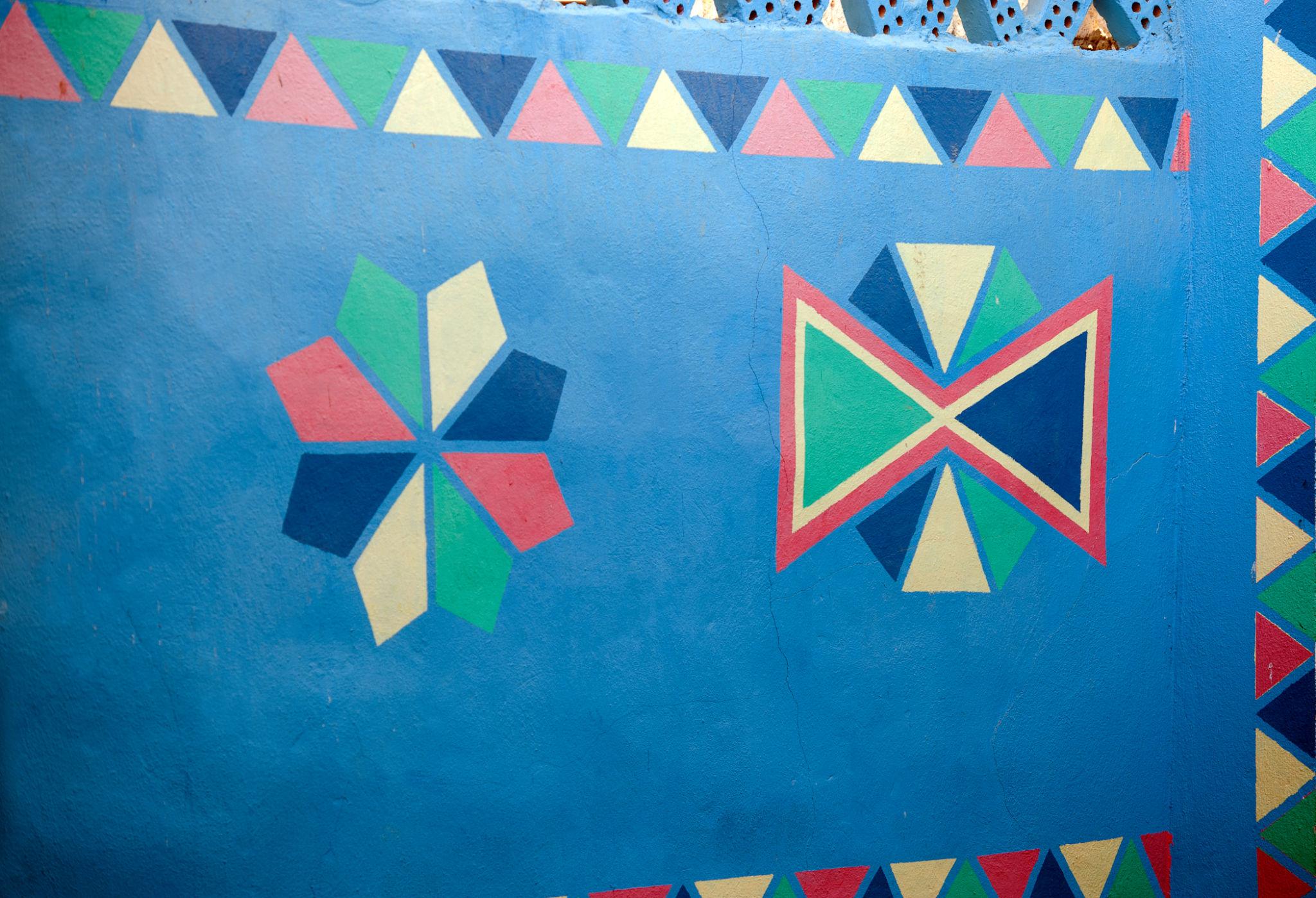 Vibrant geometric triangle and diamond patterns painted on a bright blue wall at NMEC