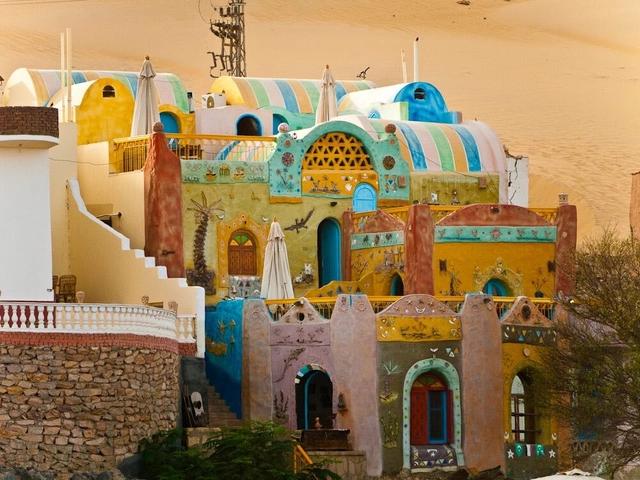 Vibrant multi-colored domed Nubian-style buildings decorated with folk art against desert sand