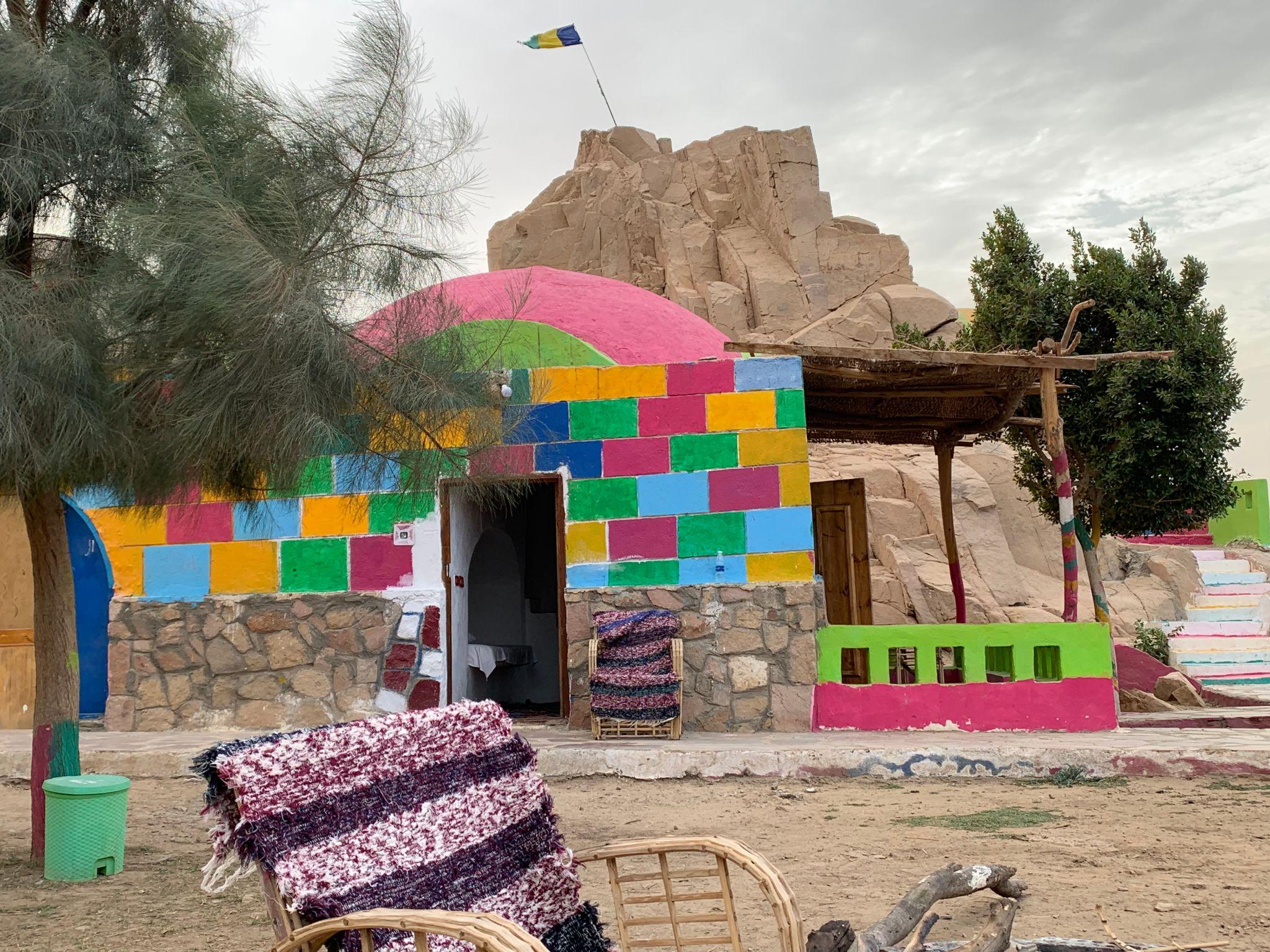 A vibrant multicolored block-painted stone building set against a rocky desert outcrop.