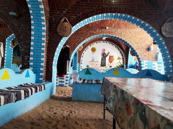 Colorful brick arches and blue walls of a traditional Nubian home exhibit with sand floor