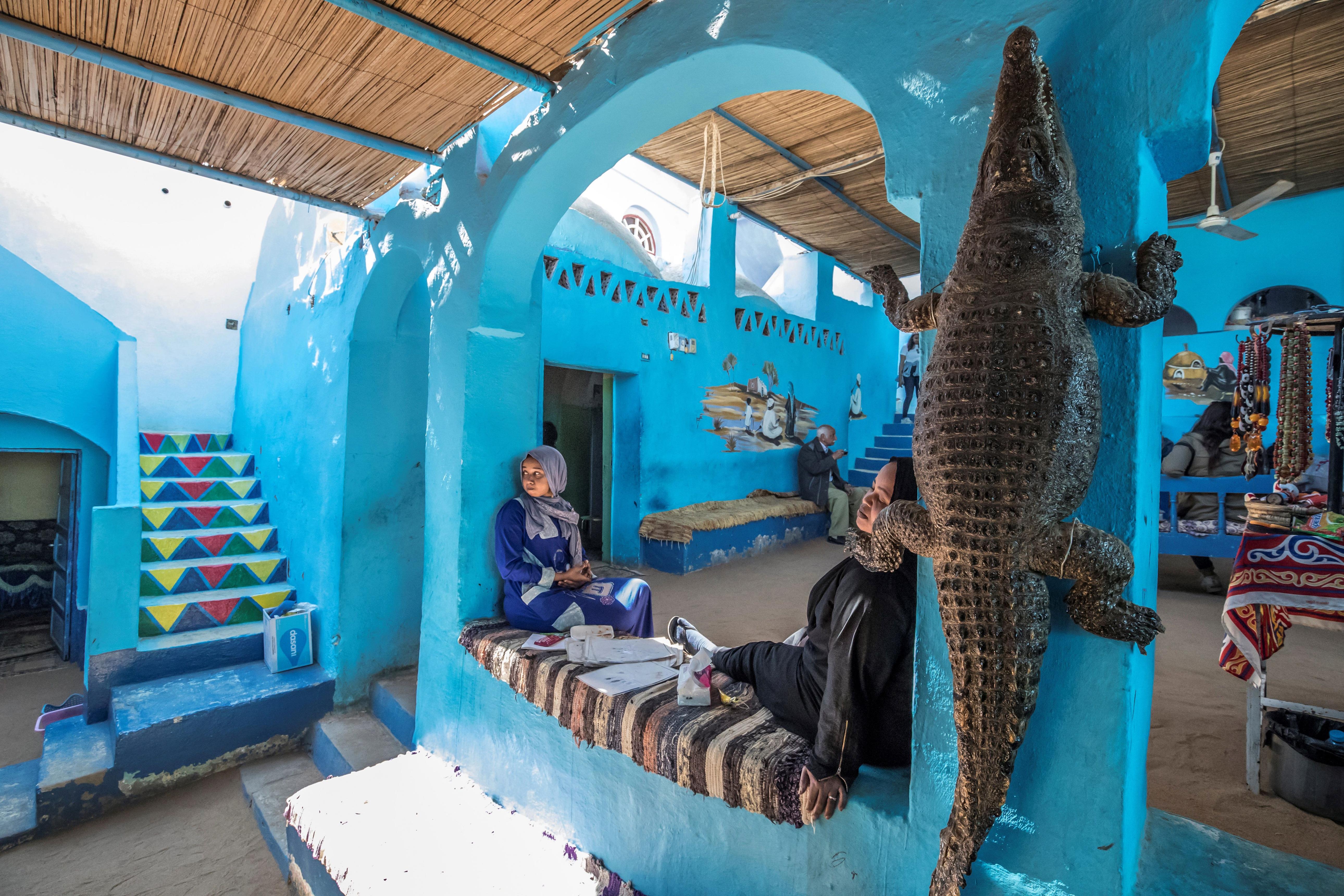 Two women relaxing in a vibrant blue Nubian house with a mounted crocodile skin on the wall