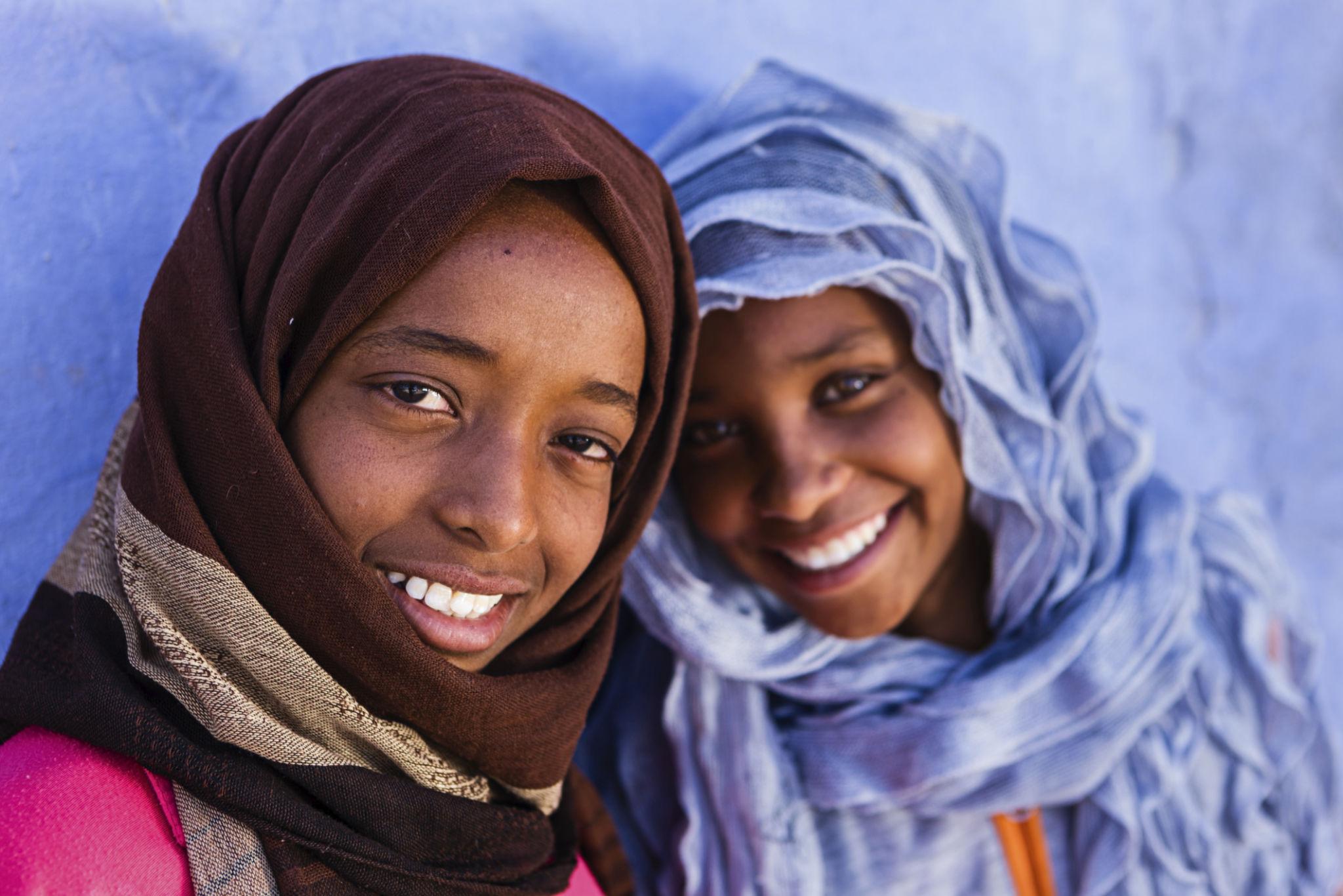Two young Egyptian girls in colorful headscarves smiling warmly at the camera
