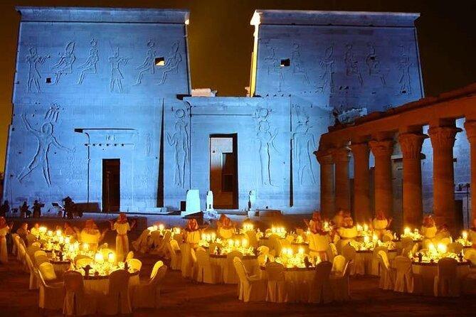Candlelit gala dinner set before the blue-lit carved façade of Philae Temple at night