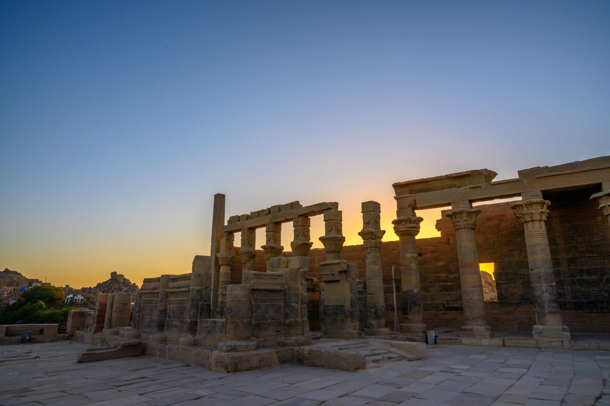 Ancient Philae Temple colonnades and stone walls silhouetted against a warm golden sunset sky