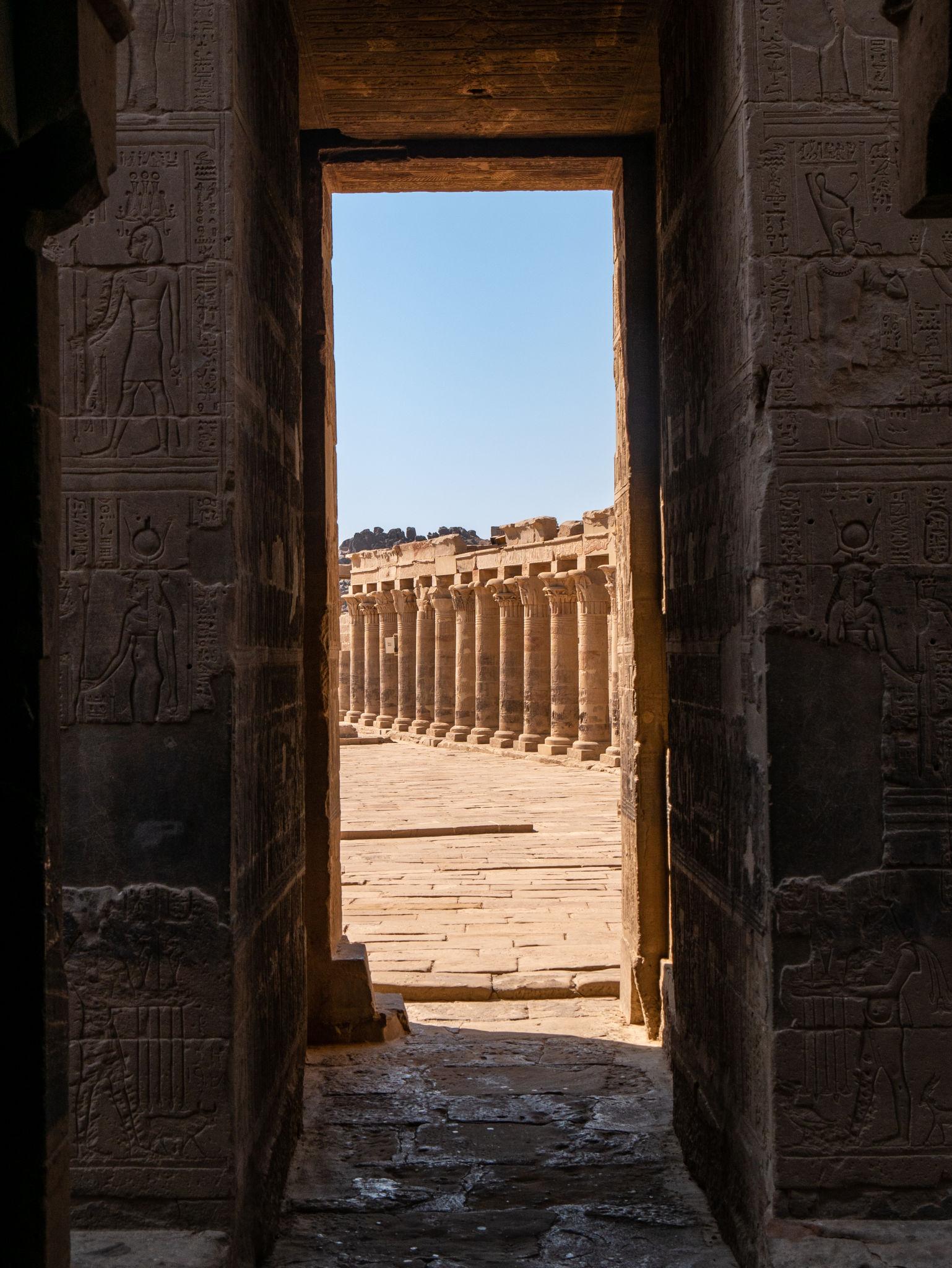 View through a hieroglyph-carved doorway into Philae Temple's sunlit colonnaded courtyard