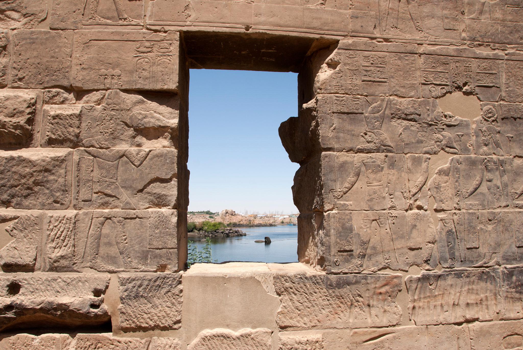 Ancient Egyptian hieroglyph-carved stone wall with a rectangular window overlooking the Nile River