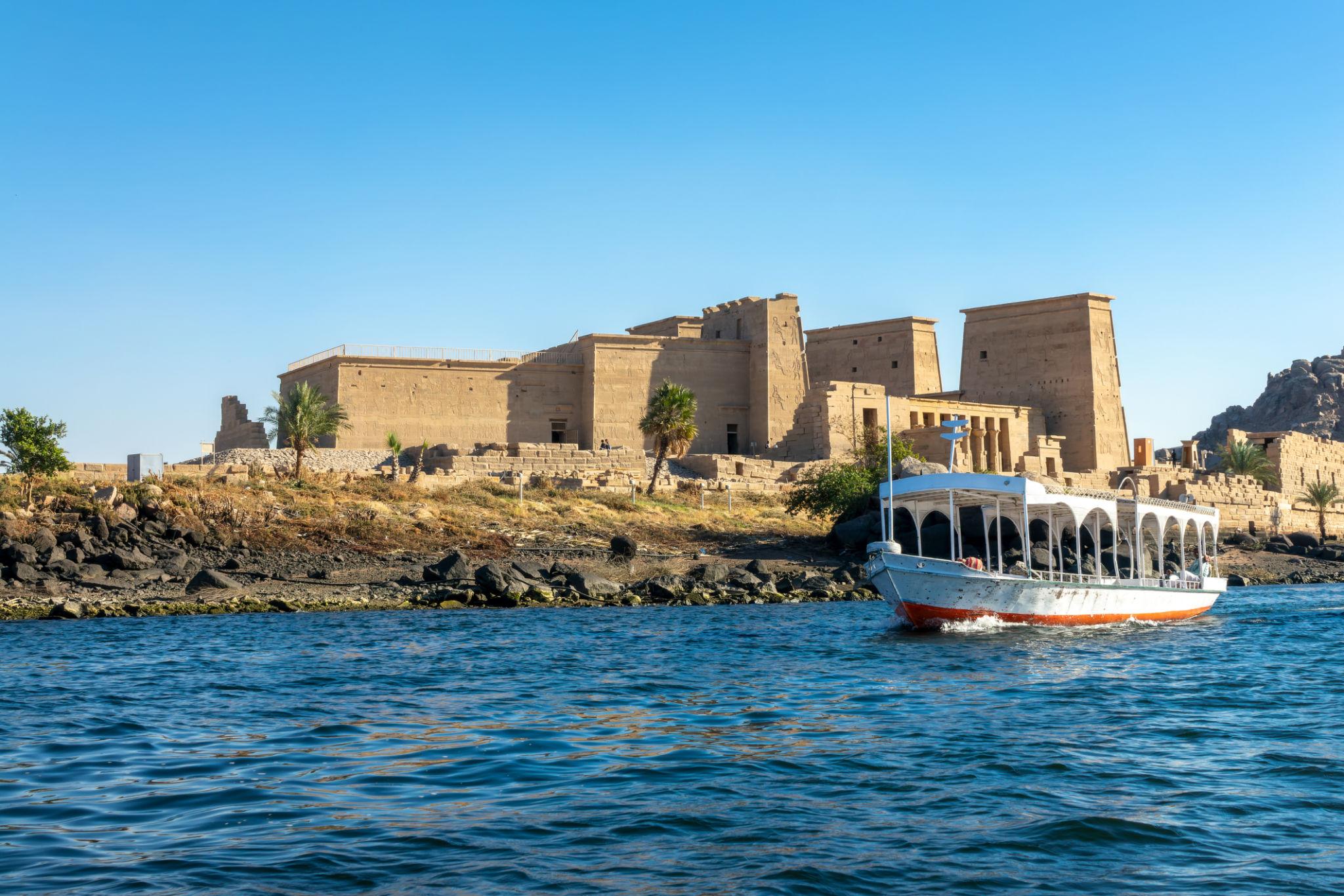 A tourist boat on the Nile with the ancient Philae Temple of Isis rising behind it