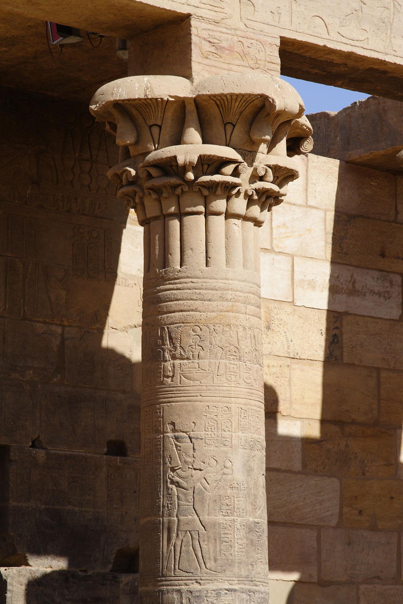 A carved stone column at Philae Temple with floral capital and hieroglyphic reliefs of Egyptian figures