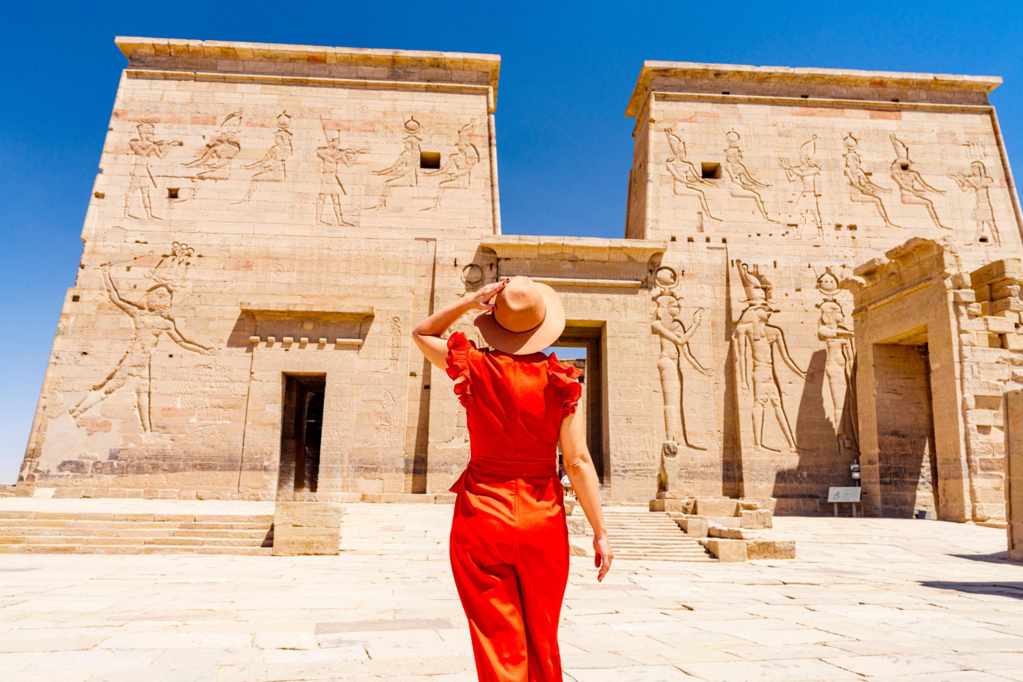 Woman in red outfit facing the carved hieroglyphic pylons of Philae Temple, Egypt