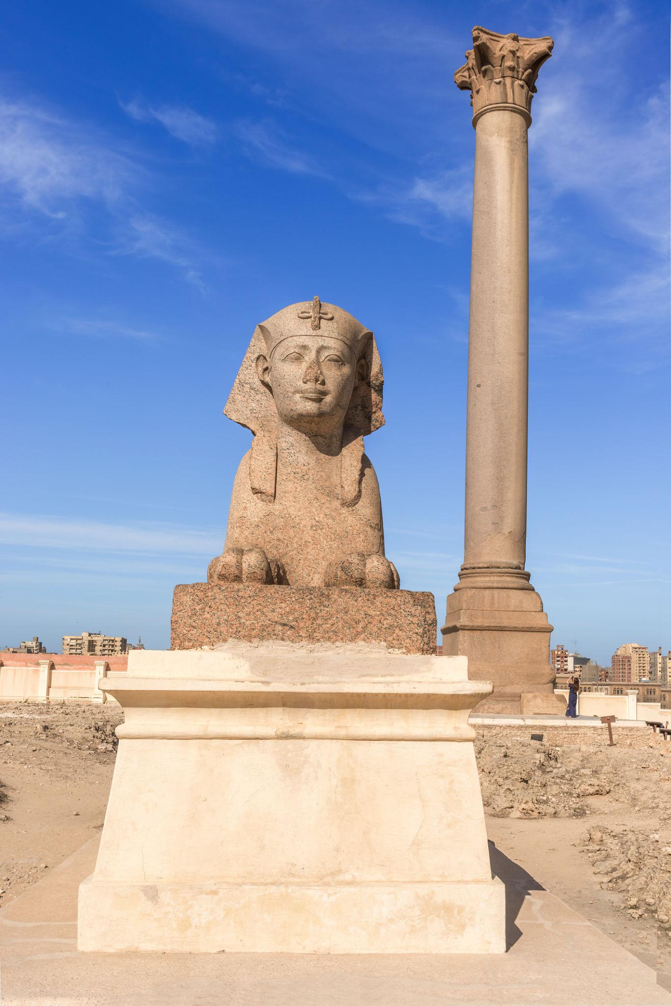 Pharaonic sphinx on pedestal beside the towering Pompey's Pillar in Alexandria