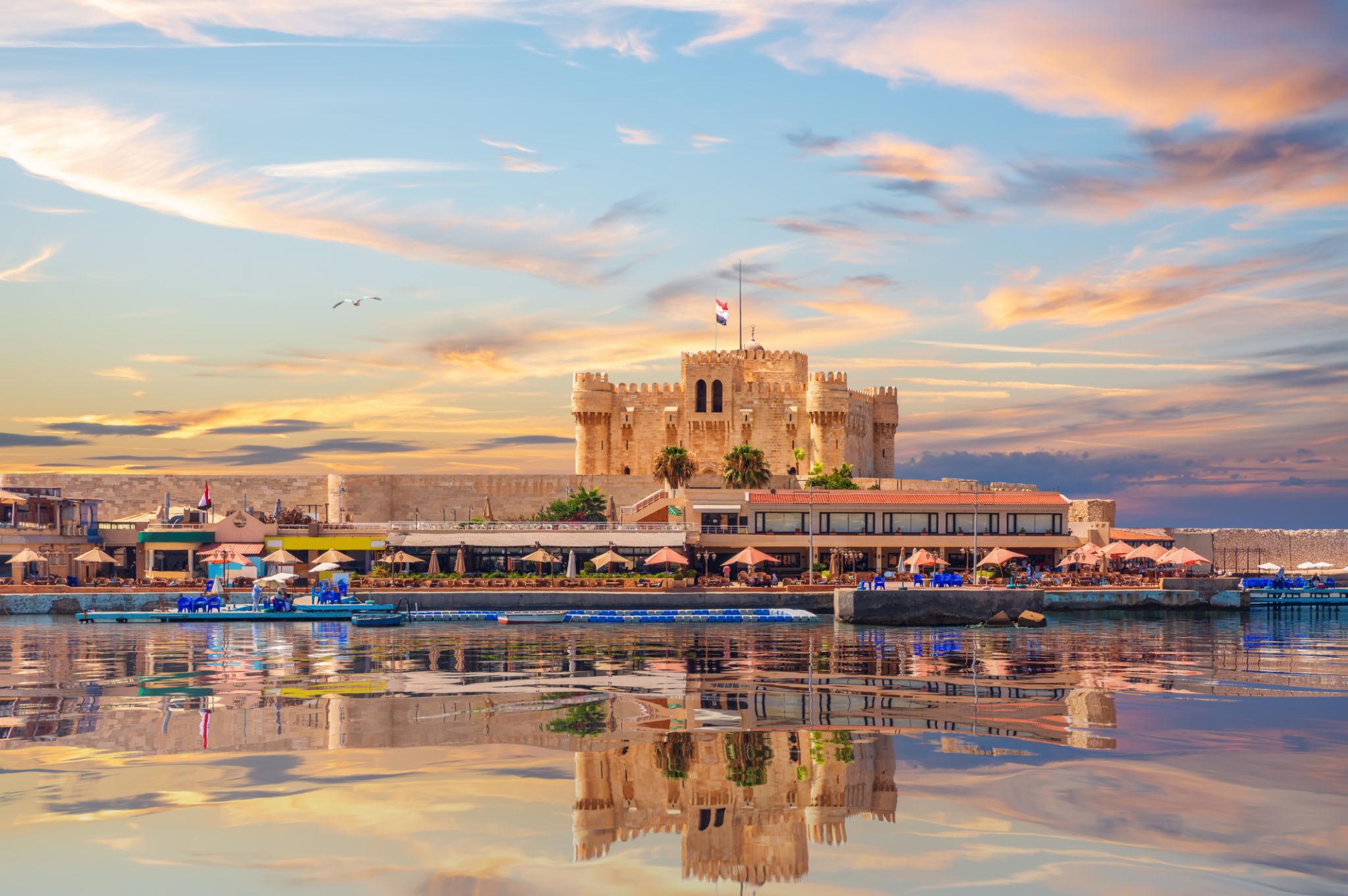 Qaitbay Citadel at sunset mirrored on calm Alexandria harbor waters with pastel sky