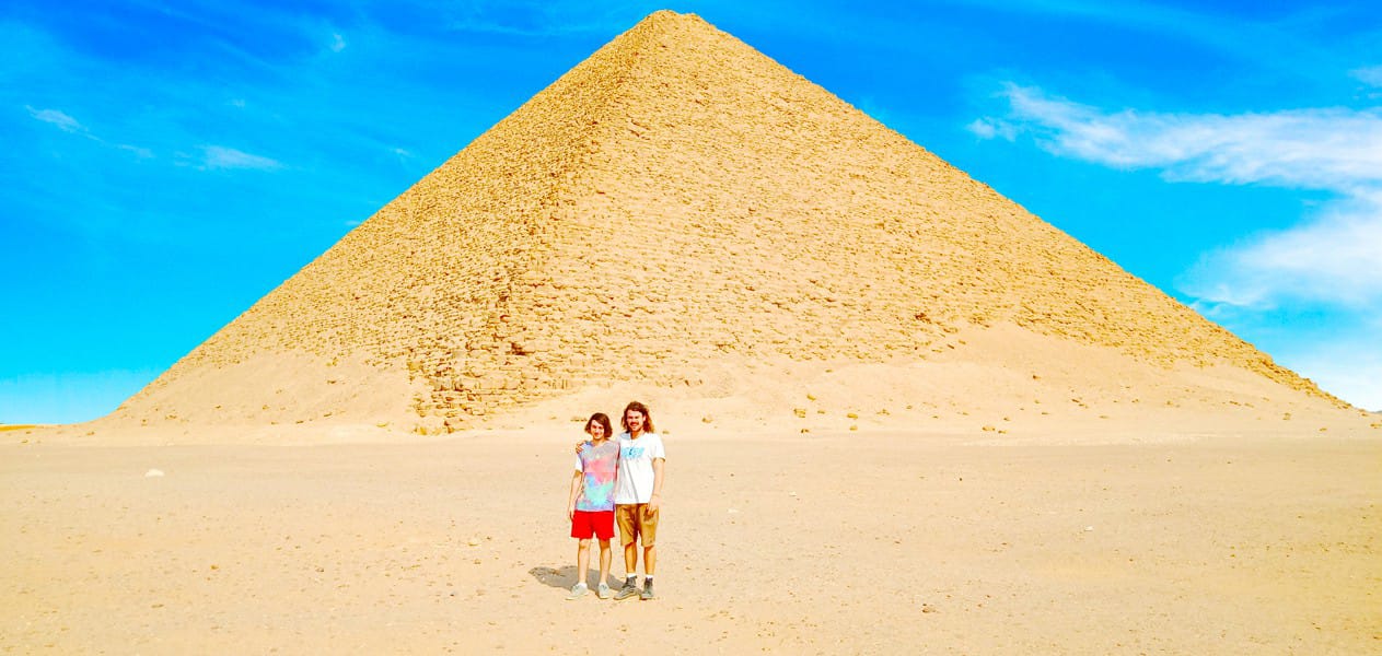 Two tourists posing in the sandy desert in front of the Red Pyramid of Dahshur.