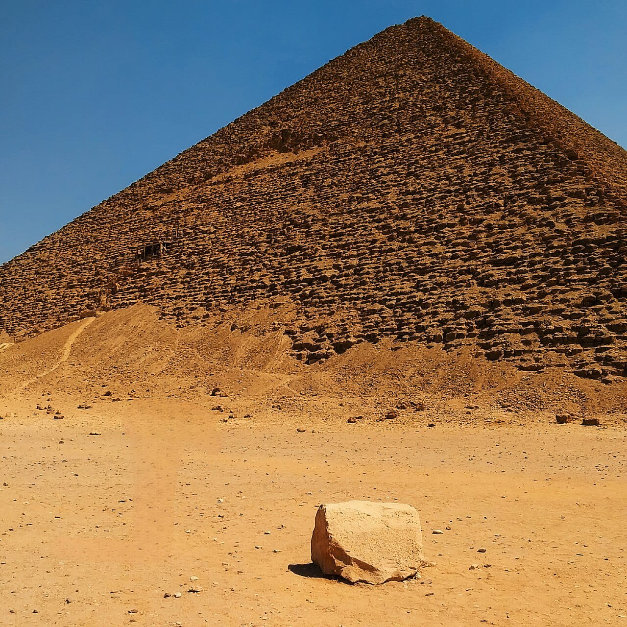 The Red Pyramid of Dahshur rising above sandy desert with a lone limestone block in the foreground.