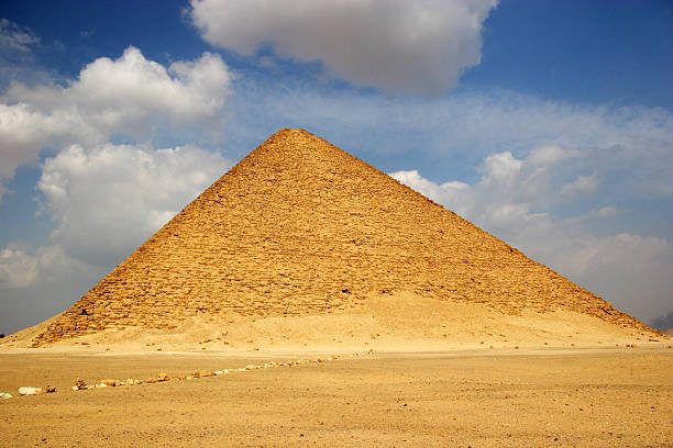 The Red Pyramid of Dahshur rising from golden desert sands under a partly cloudy blue sky.