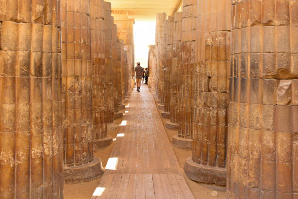 Tourists walking between tall ancient stone columns in the Serapeum of Saqqara, Egypt