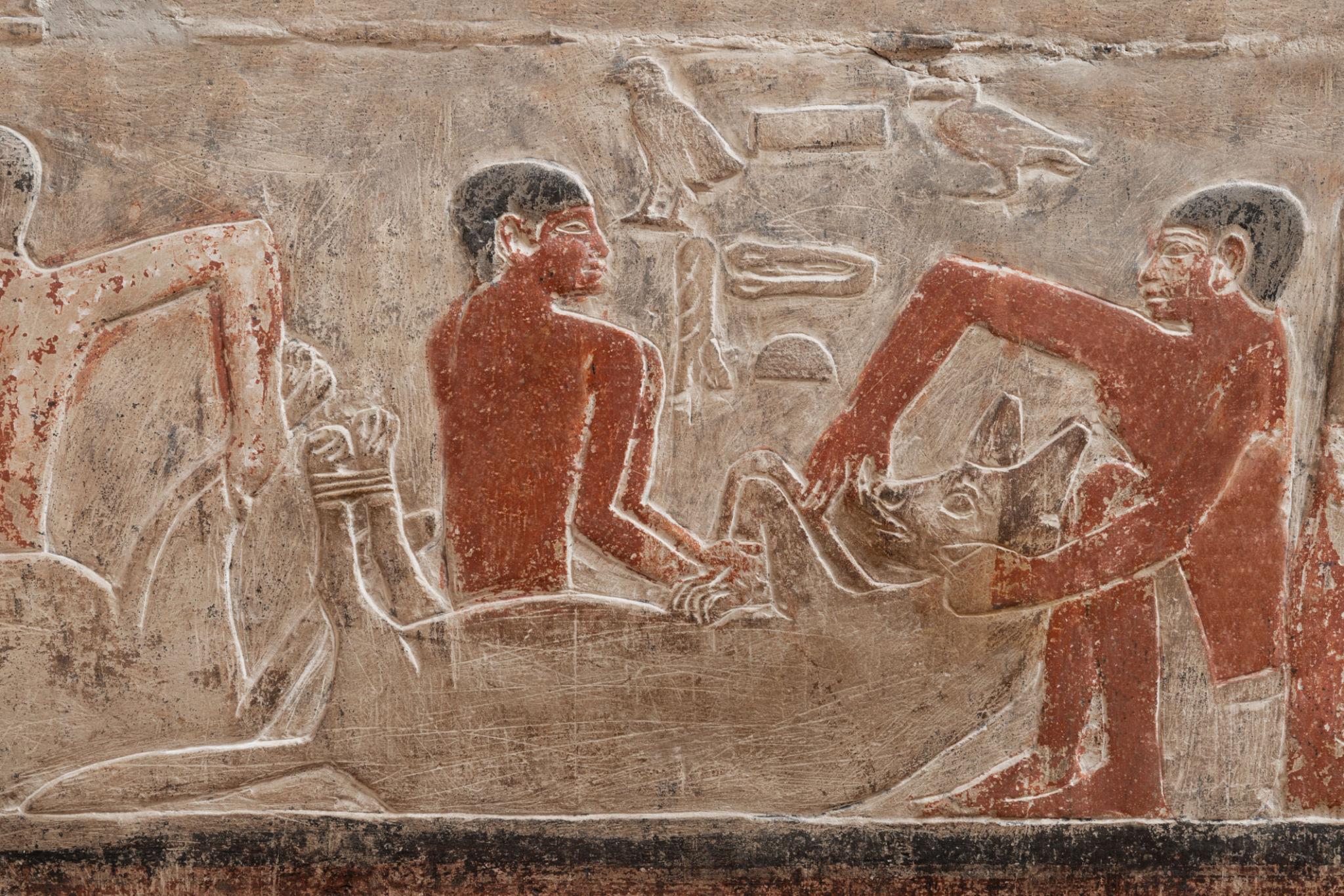 Ancient Egyptian painted limestone relief showing three figures engaged in craftwork or ritual activity