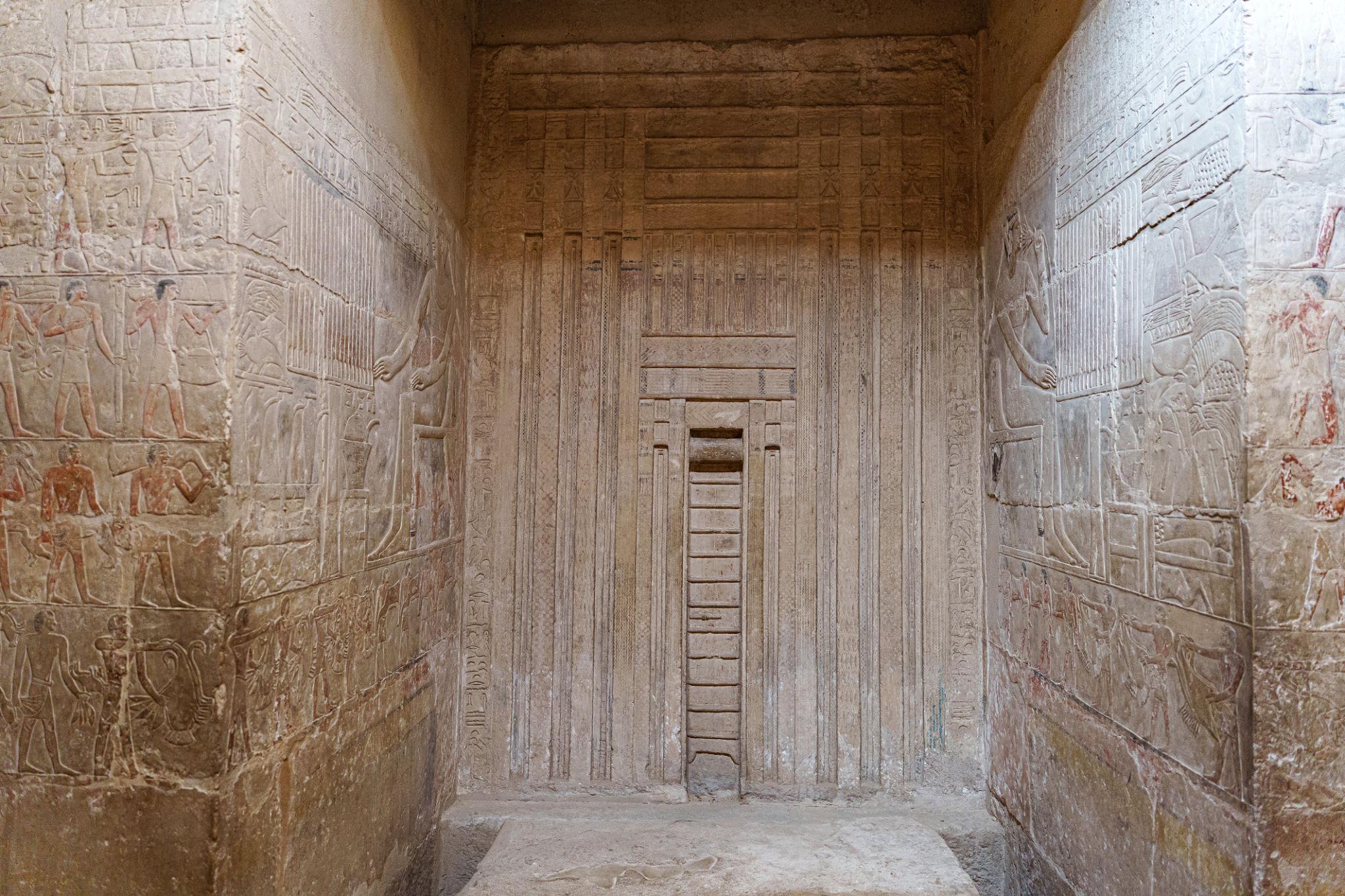 Ancient Egyptian false door stela flanked by carved hieroglyphic reliefs inside a tomb chapel