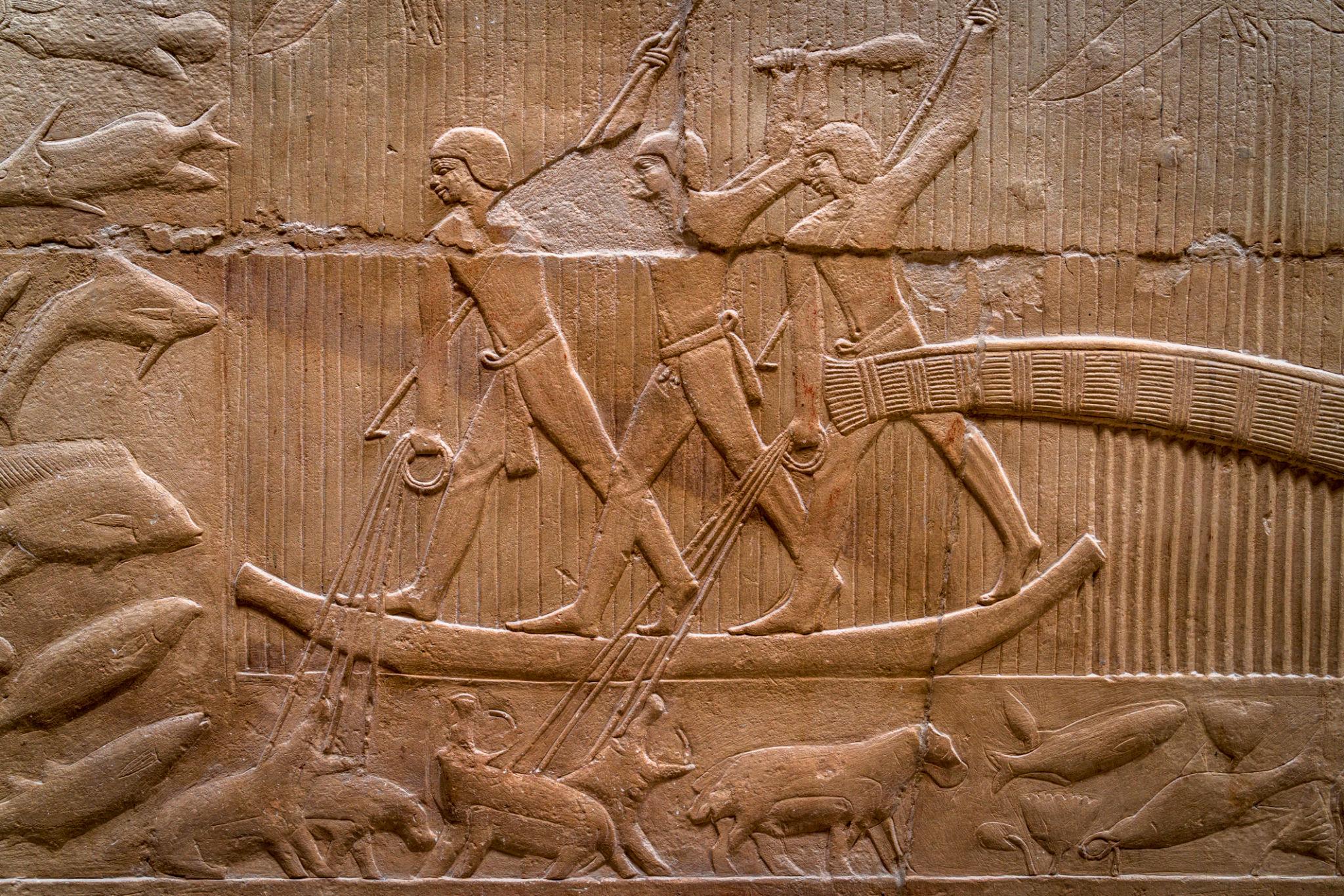 Ancient Egyptian stone relief showing fishermen standing in a papyrus boat with fish and animals below