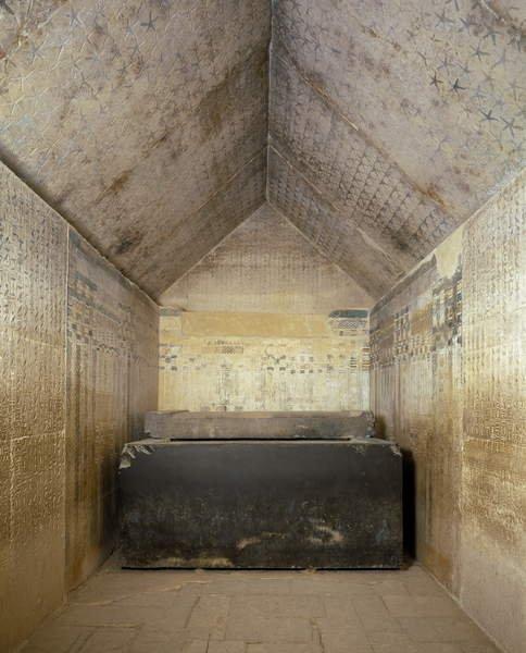 Massive dark granite sarcophagus inside a painted hieroglyph-covered burial chamber at Saqqara