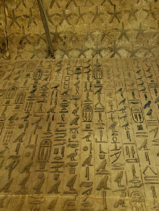 Ancient Egyptian hieroglyphs carved into a stone wall with star decorations above