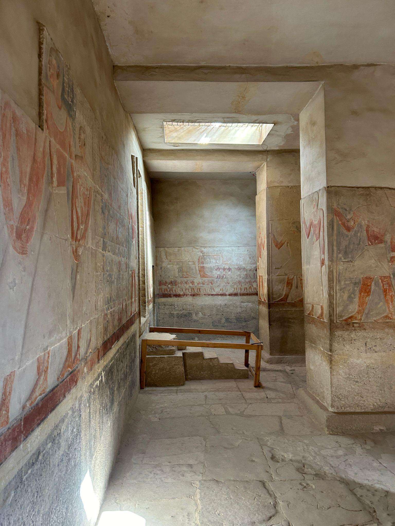 Ancient Egyptian painted figures on limestone walls of a tomb corridor with skylight above
