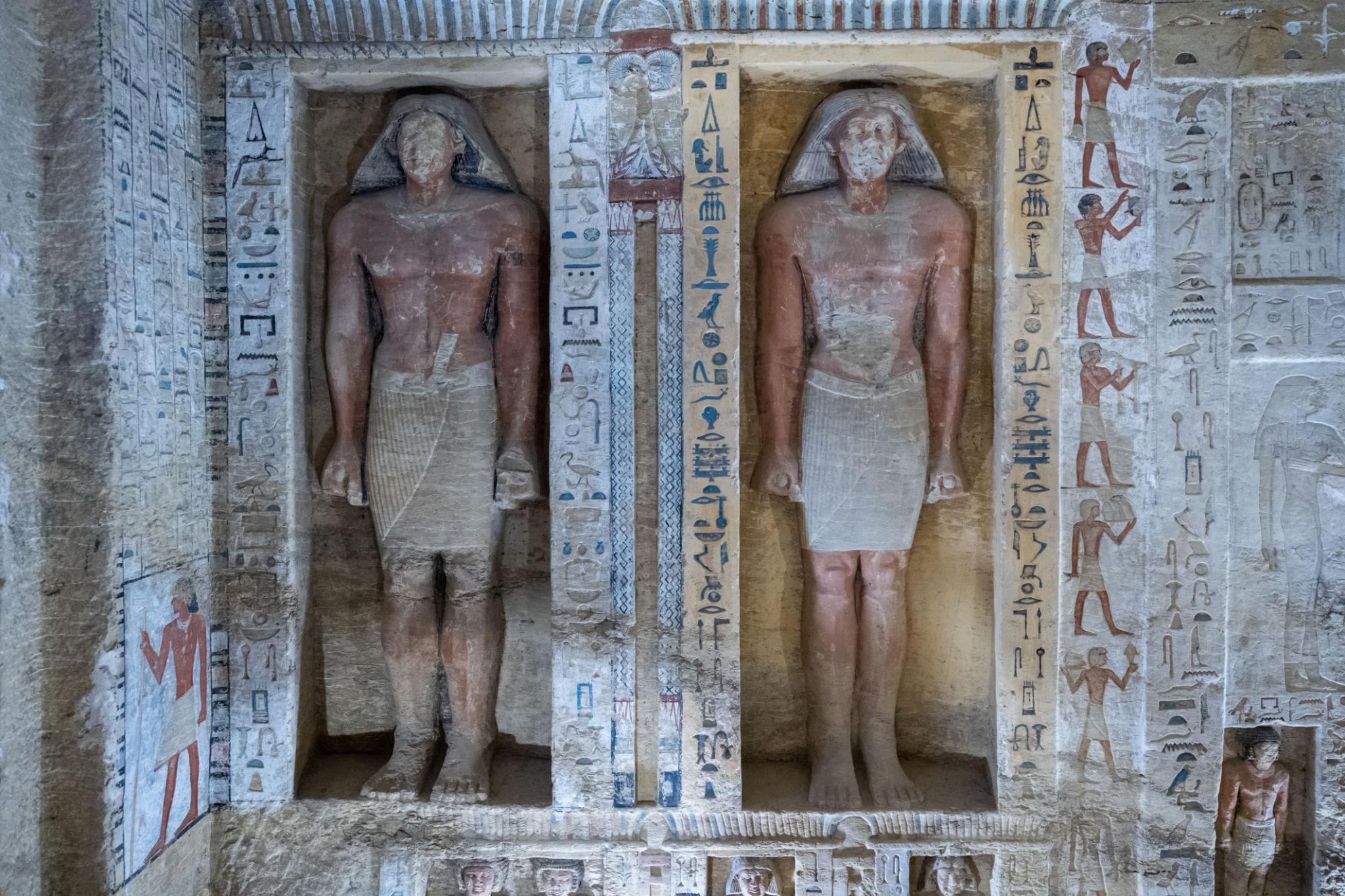 Two ancient Egyptian painted relief statues in carved niches surrounded by colorful hieroglyphs
