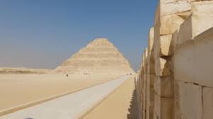 The Step Pyramid of Djoser seen from a stone-lined corridor at Saqqara under a clear blue sky