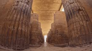 Massive ancient Egyptian carved stone columns lining a narrow corridor at Saqqara