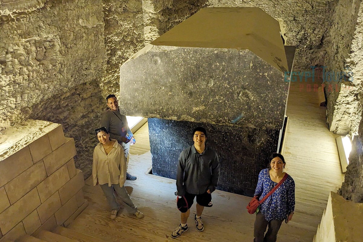 Four tourists posing beside a massive dark granite sarcophagus in the Serapeum underground vault