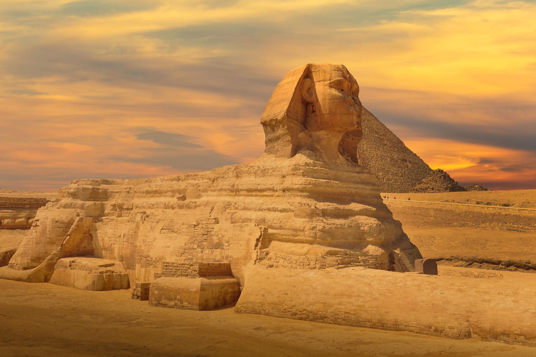 The Great Sphinx of Giza in profile at sunset with a pyramid rising behind it