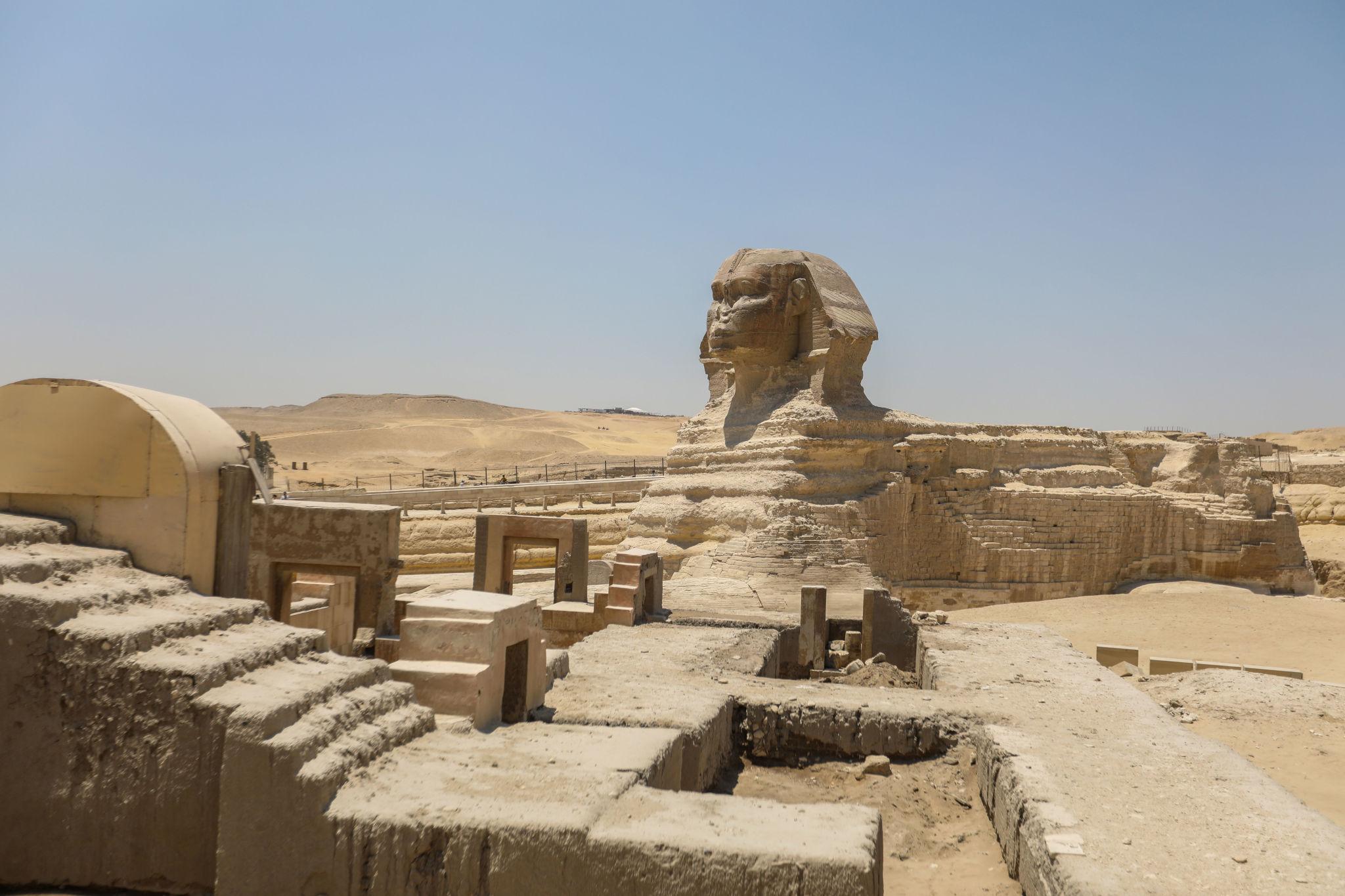 Side profile of the Great Sphinx of Giza with ancient stone ruins in the foreground.
