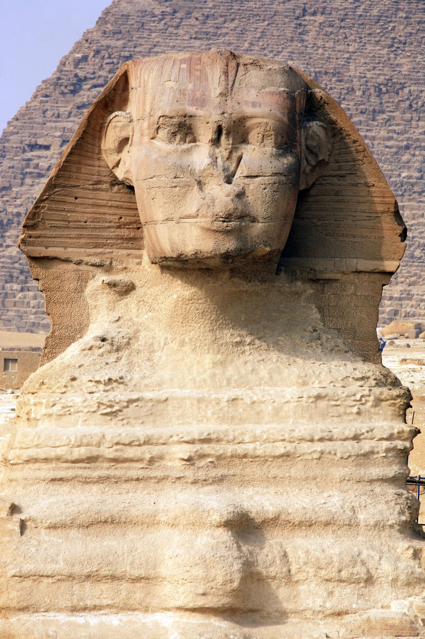 Close-up of the Great Sphinx of Giza's eroded face with a pyramid rising behind it