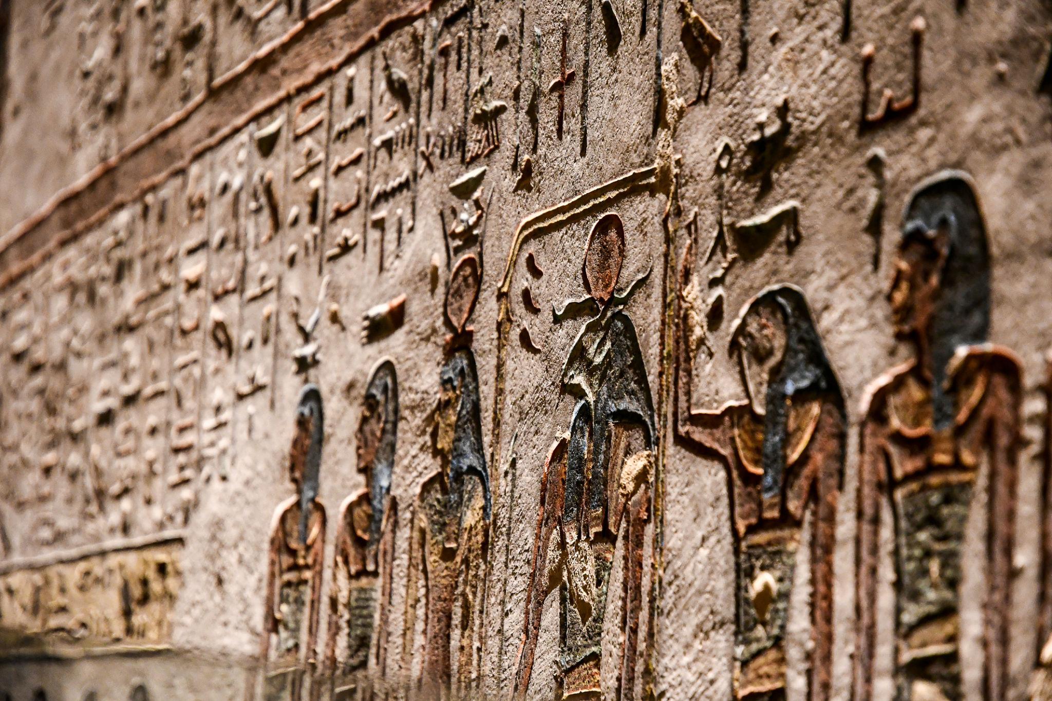 Close-up of carved wall relief showing figures and hieroglyphs in raised stone.
