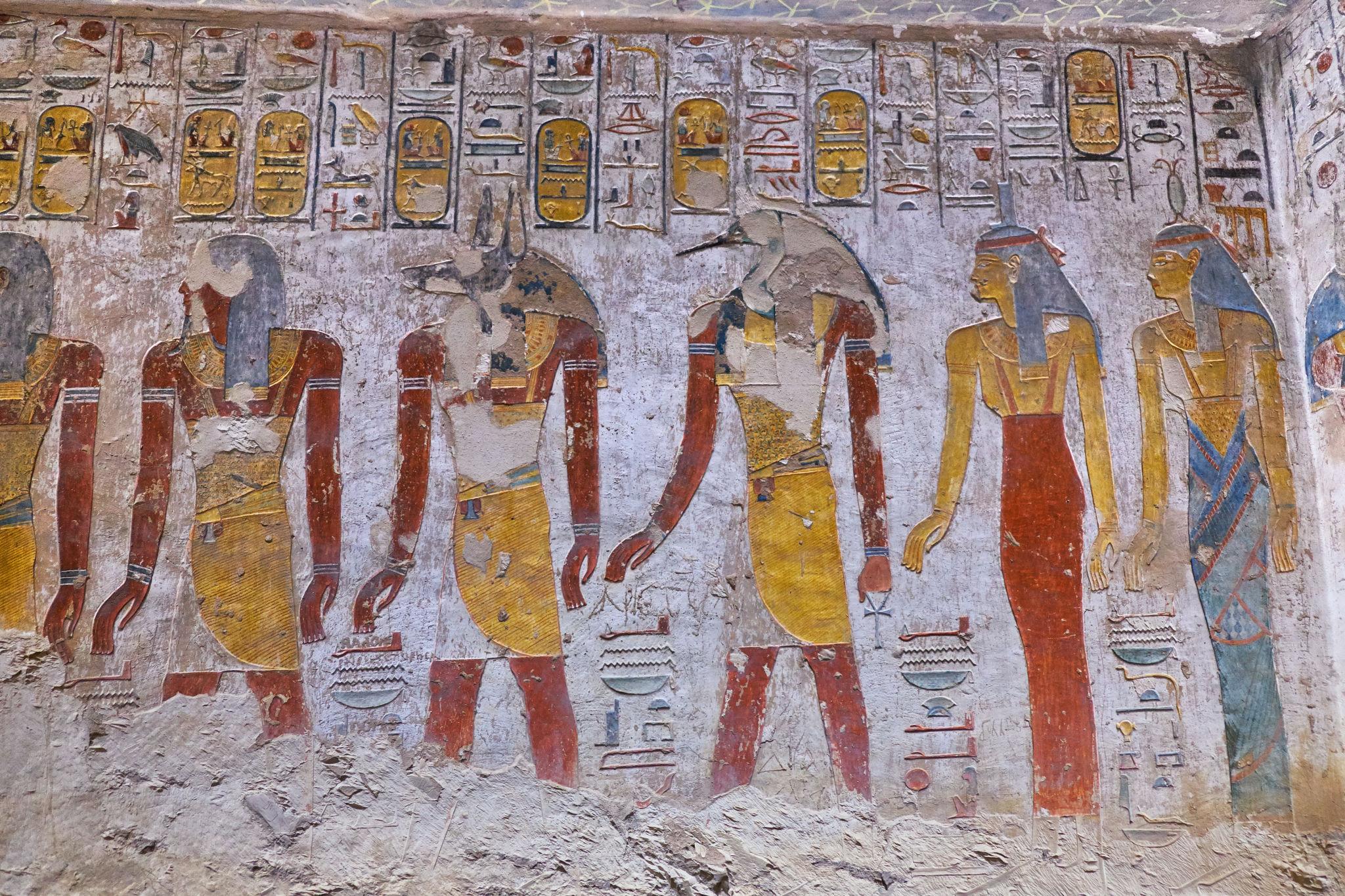 Painted row of Egyptian deities receiving offerings on a tomb wall.