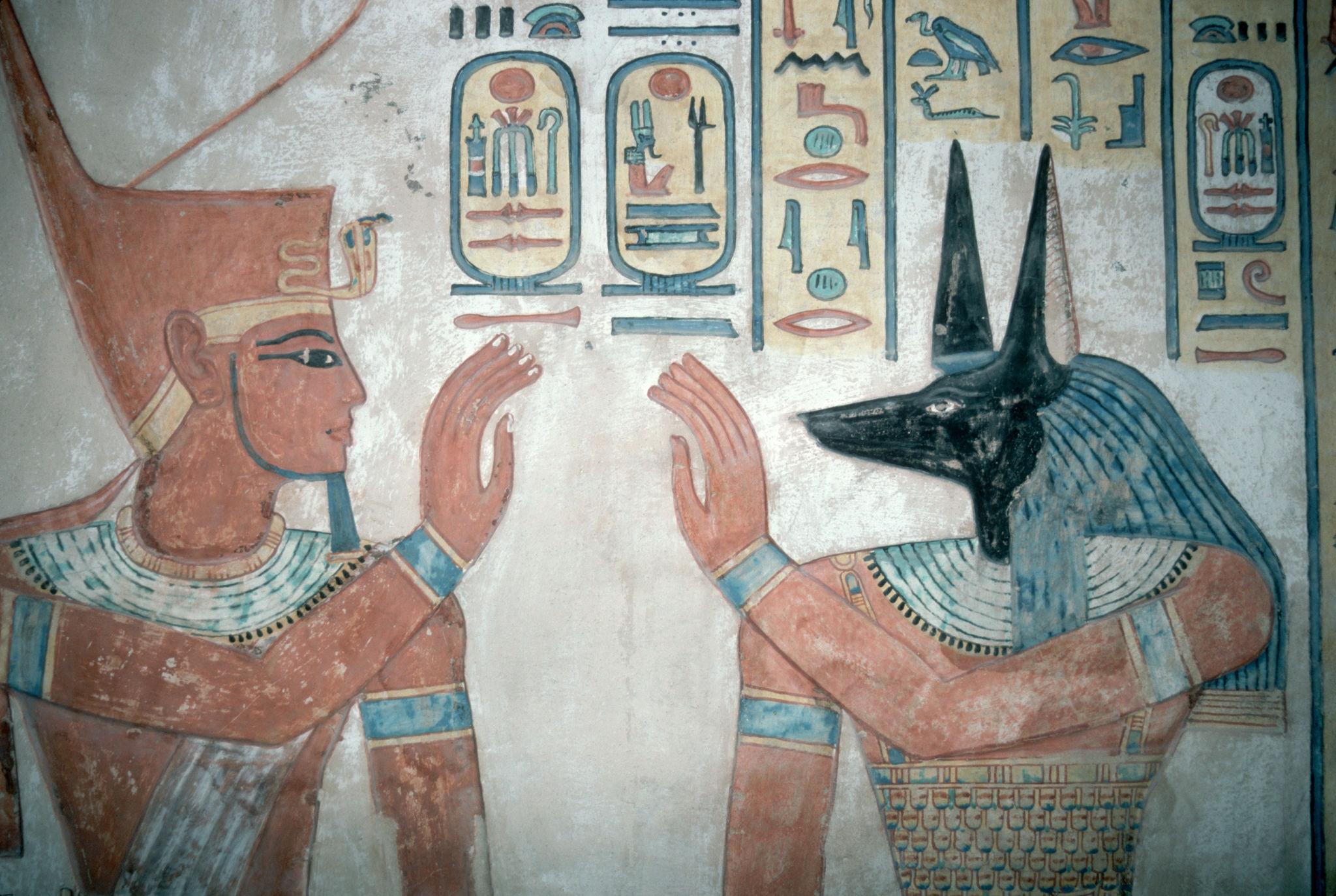 Painted scene of a pharaoh facing jackal-headed Anubis in a tomb chamber.
