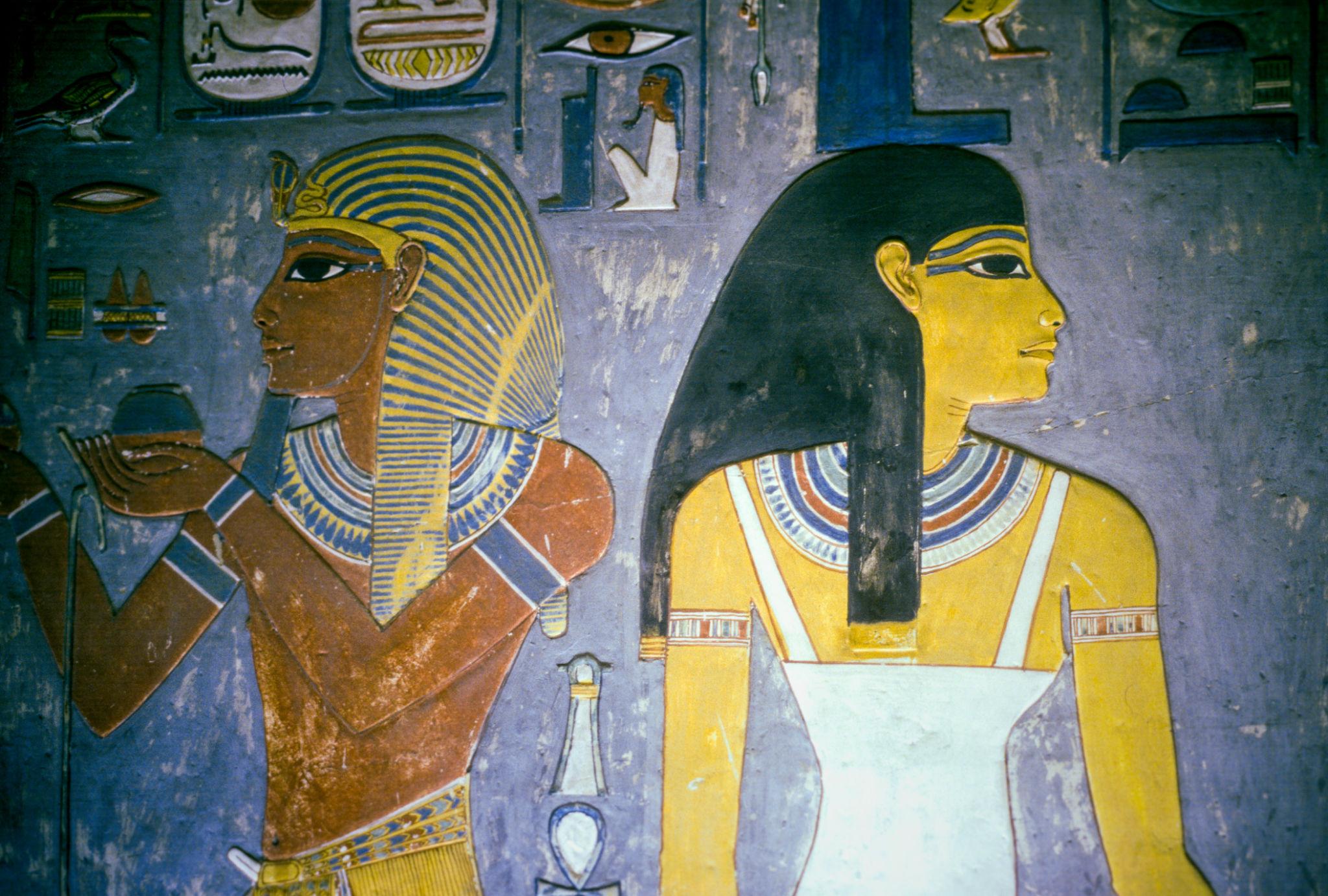 Painted pharaoh offering to a goddess on a blue-background tomb wall.