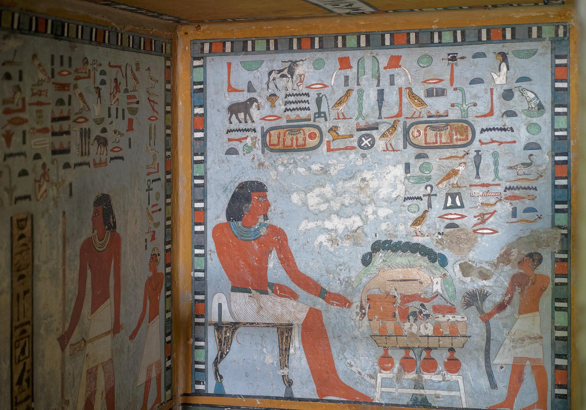 Tomb owner seated before a heaped offering table in a blue-ground mural.