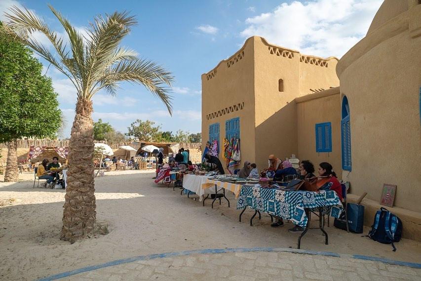 Artisans selling crafts at outdoor tables beside a mud-brick building in Tunis Village
