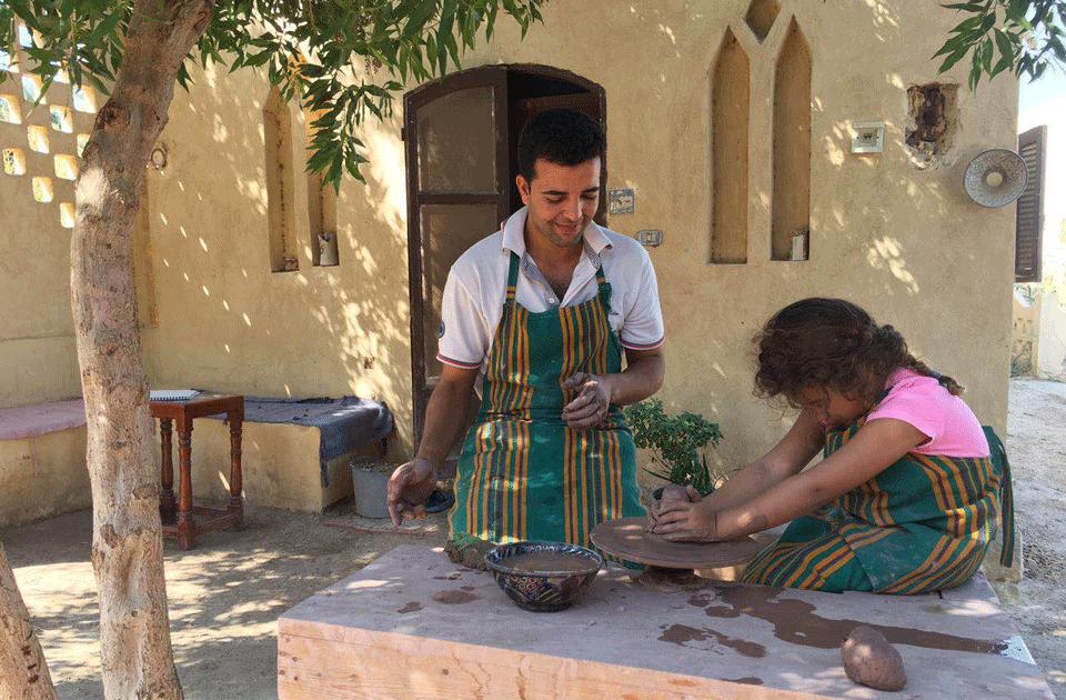 Potter teaching a child to shape clay on a wheel at a Tunis Village pottery workshop