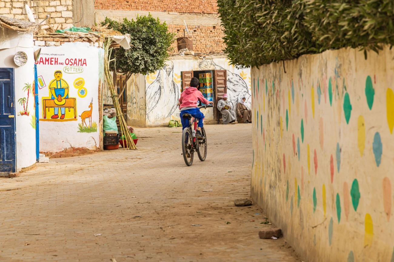 Child cycling past a Sameh and Osama pottery studio on a quiet Tunis Village lane