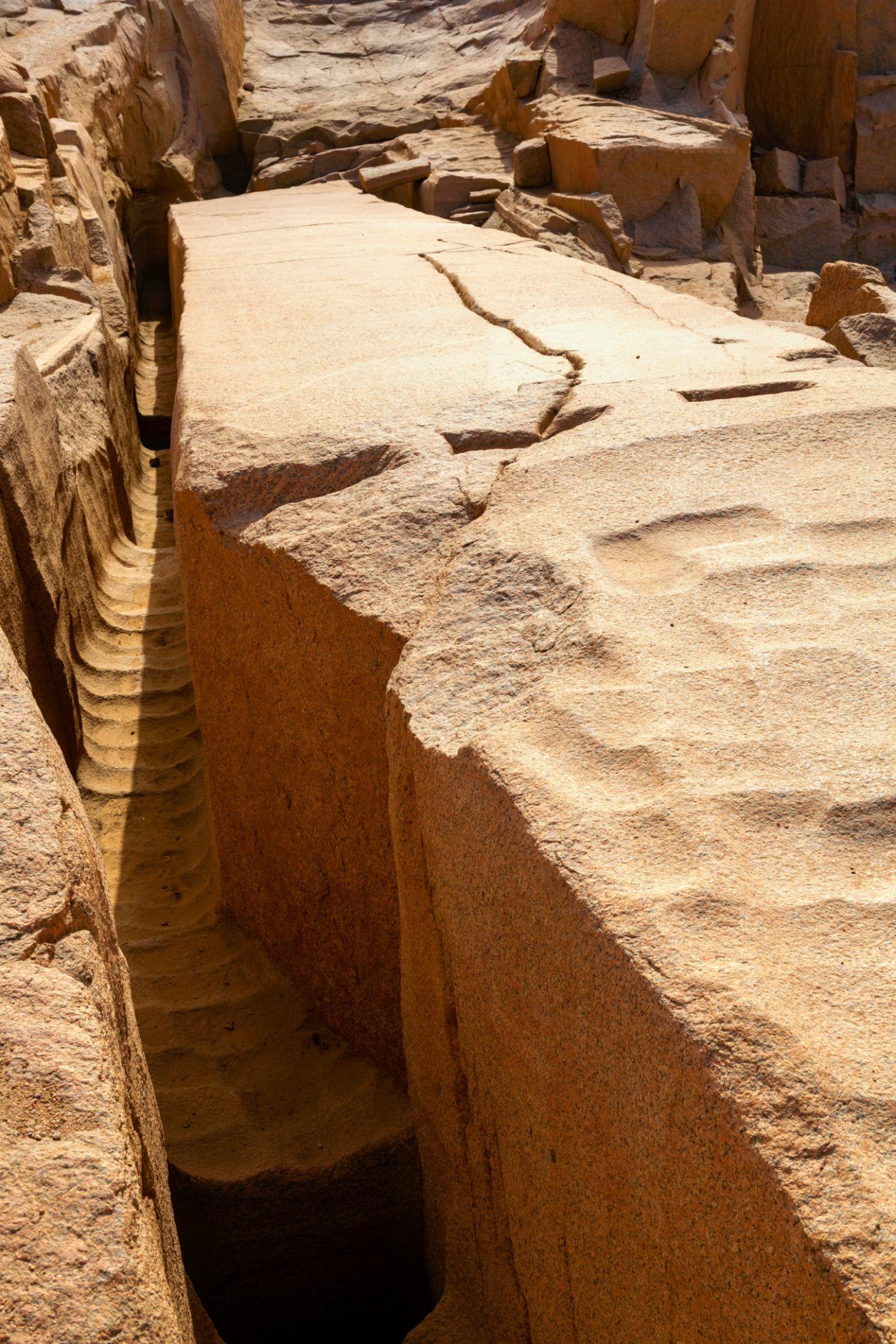 A deep carved trench beside a massive unfinished granite obelisk in an ancient Egyptian quarry