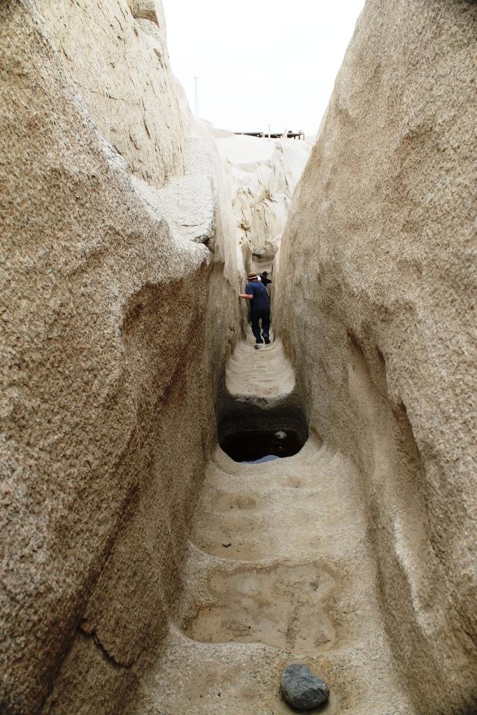 A person navigates a narrow rock-cut corridor in the ancient granite quarry of the Unfinished Obelisk