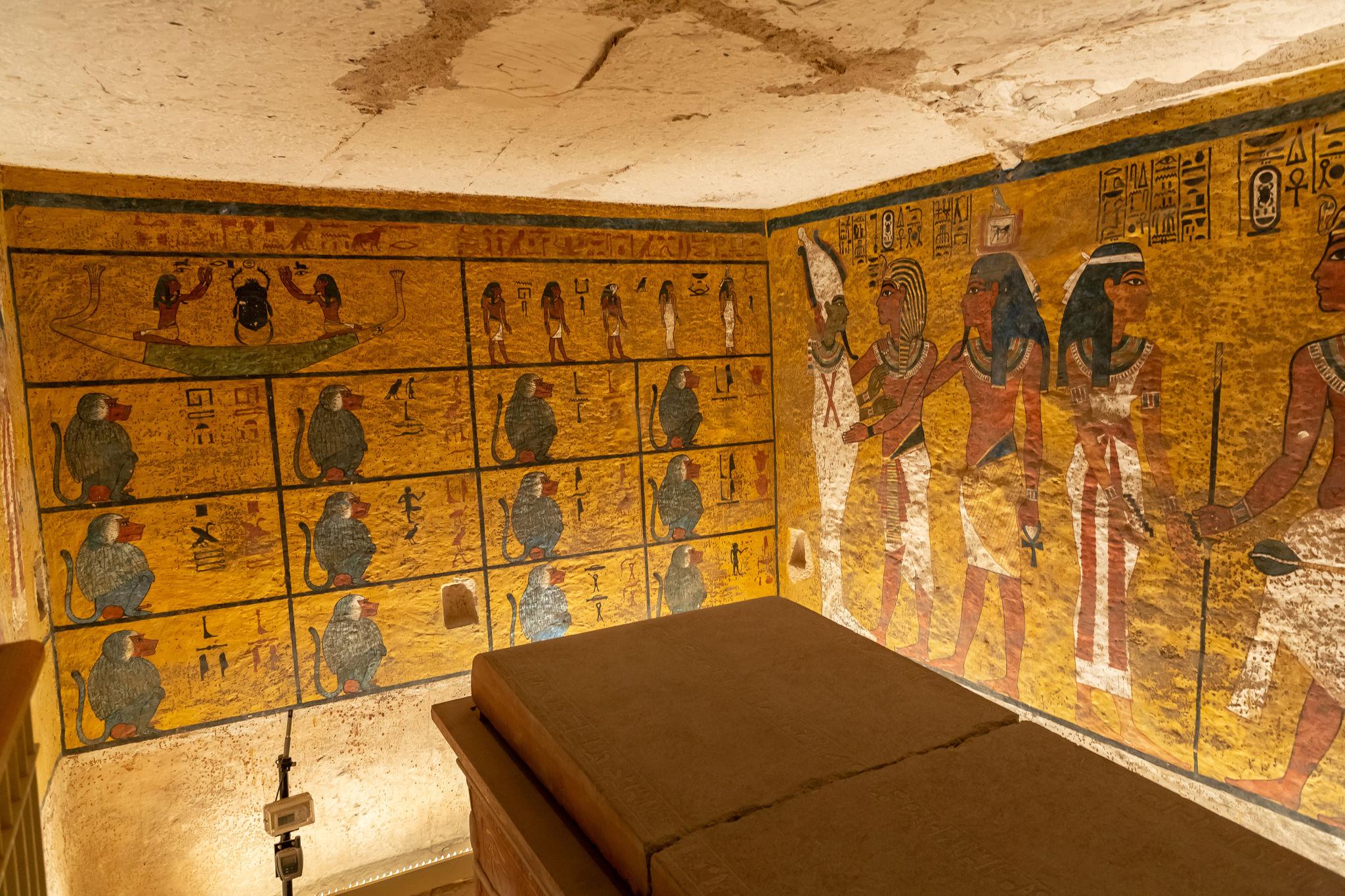 Painted walls of baboons and deities surrounding a sarcophagus plinth inside a royal tomb.