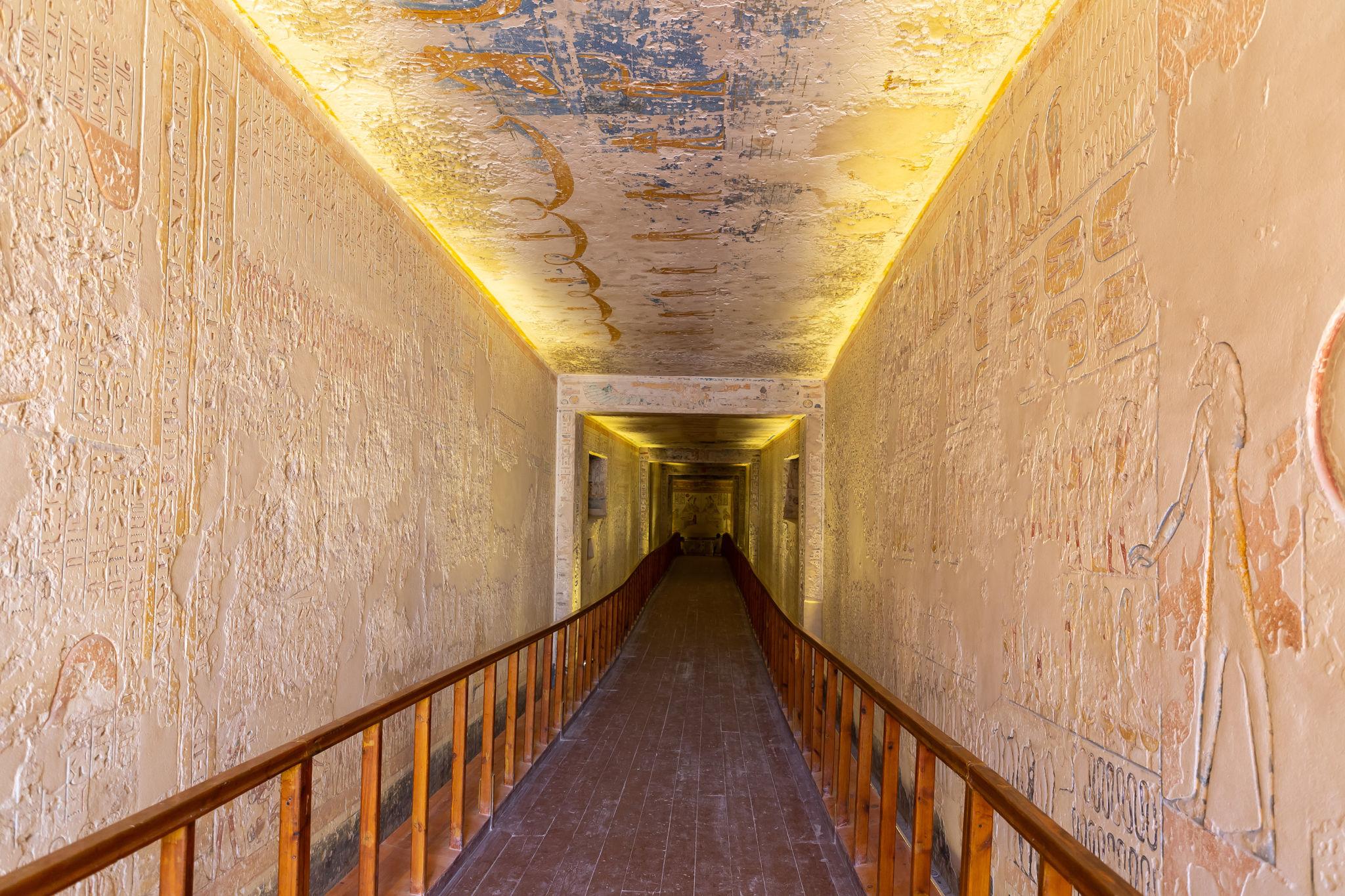 Long descending corridor with carved reliefs leading deep into a royal tomb.