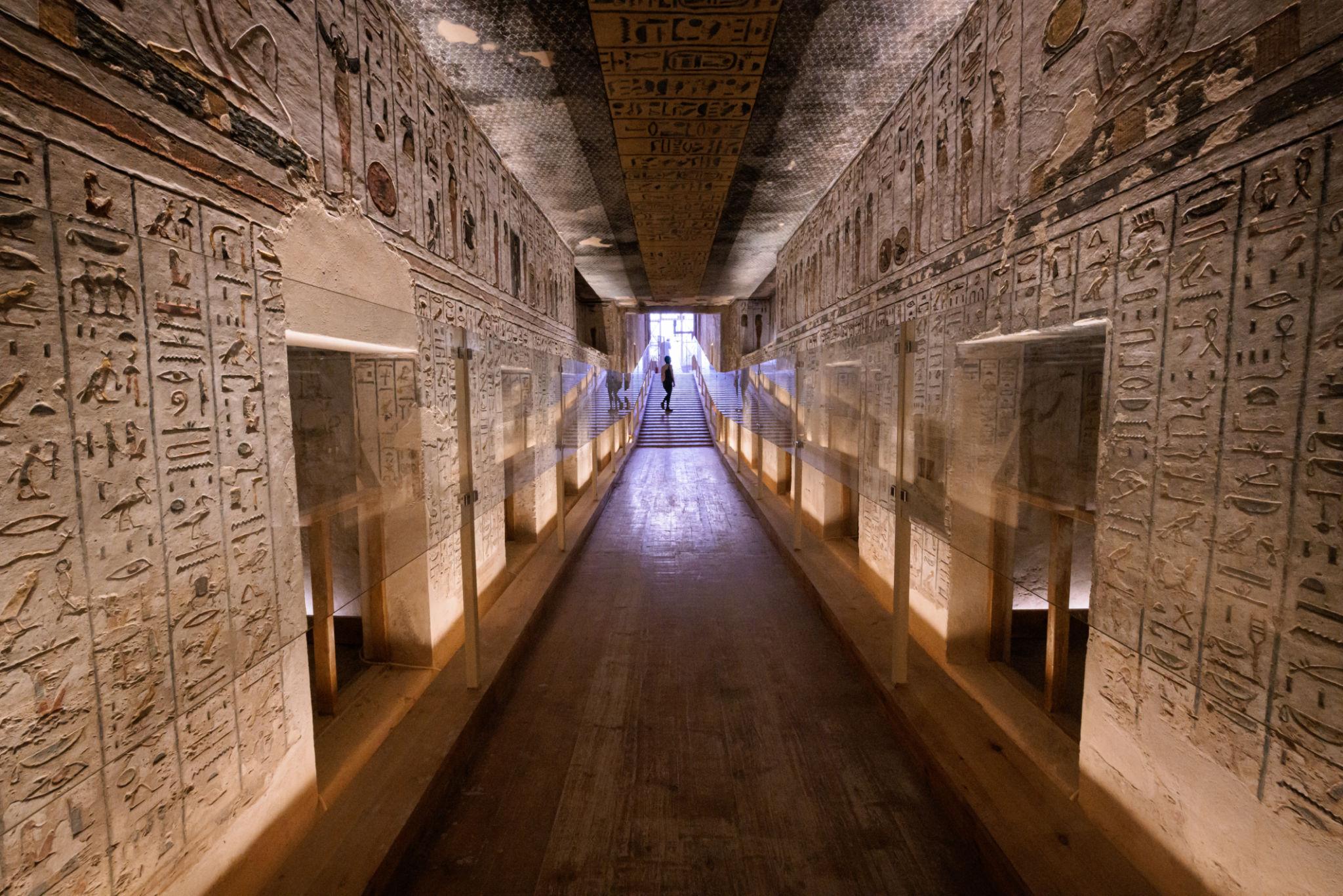 Long illuminated tomb corridor lined with dense hieroglyph inscriptions and niches.
