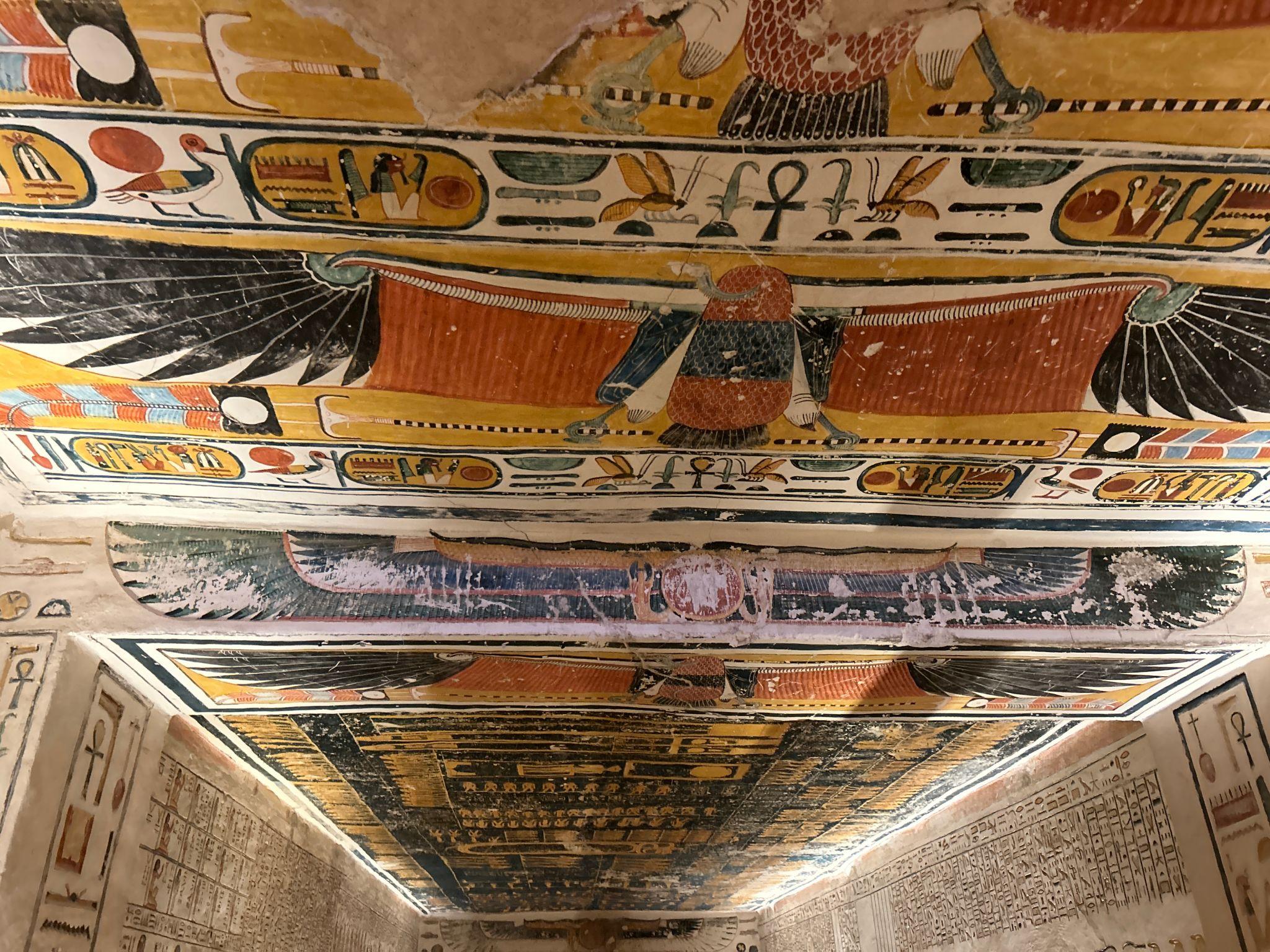 Sky goddess Nut painted along a tomb ceiling surrounded by solar deities and hieroglyphs.