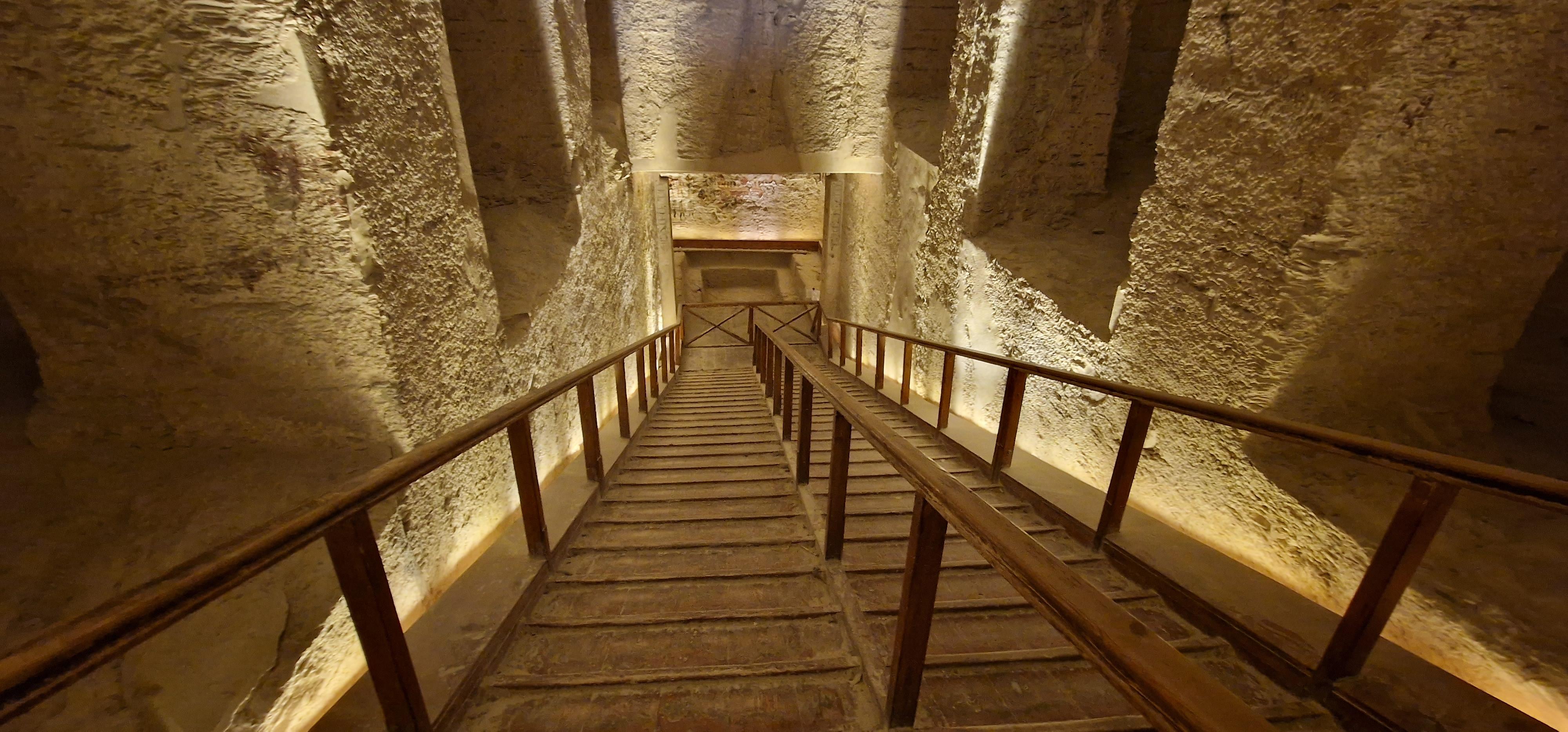 Steep wooden stairway descending through a rough-cut limestone shaft inside a tomb.