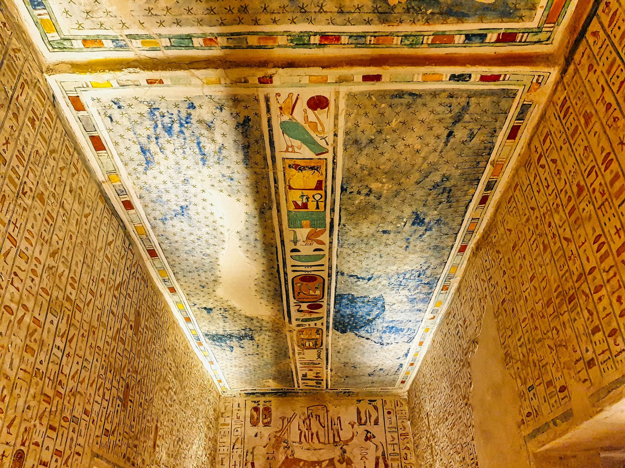 Blue star-painted ceiling rising above hieroglyph-inscribed walls in a Valley of the Kings corridor.