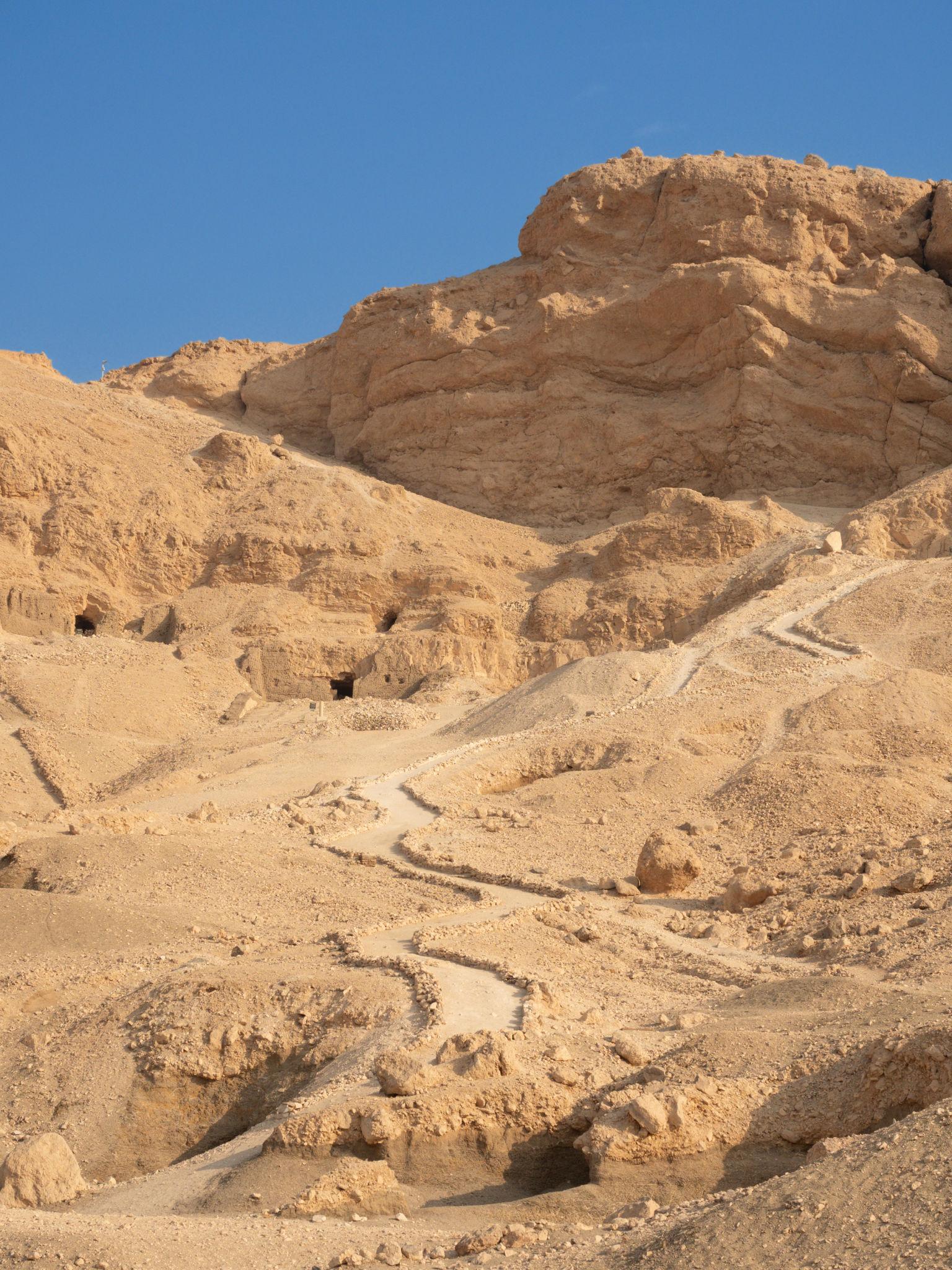 Desert hillside dotted with tomb openings and access paths in the Valley of the Kings.